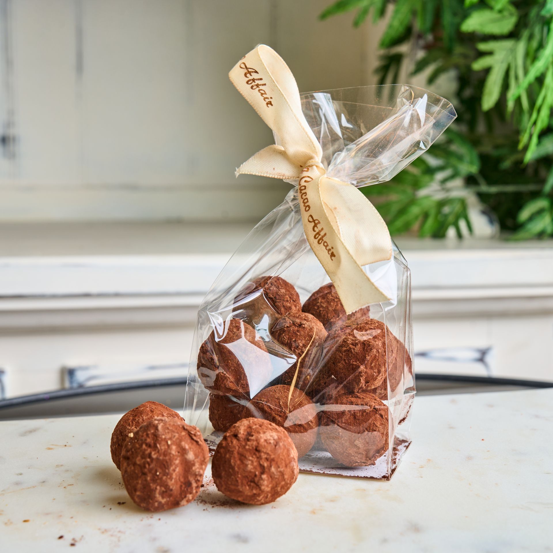 Chocolate truffles in a clear bag tied with a cream ribbon, set on a marble surface.