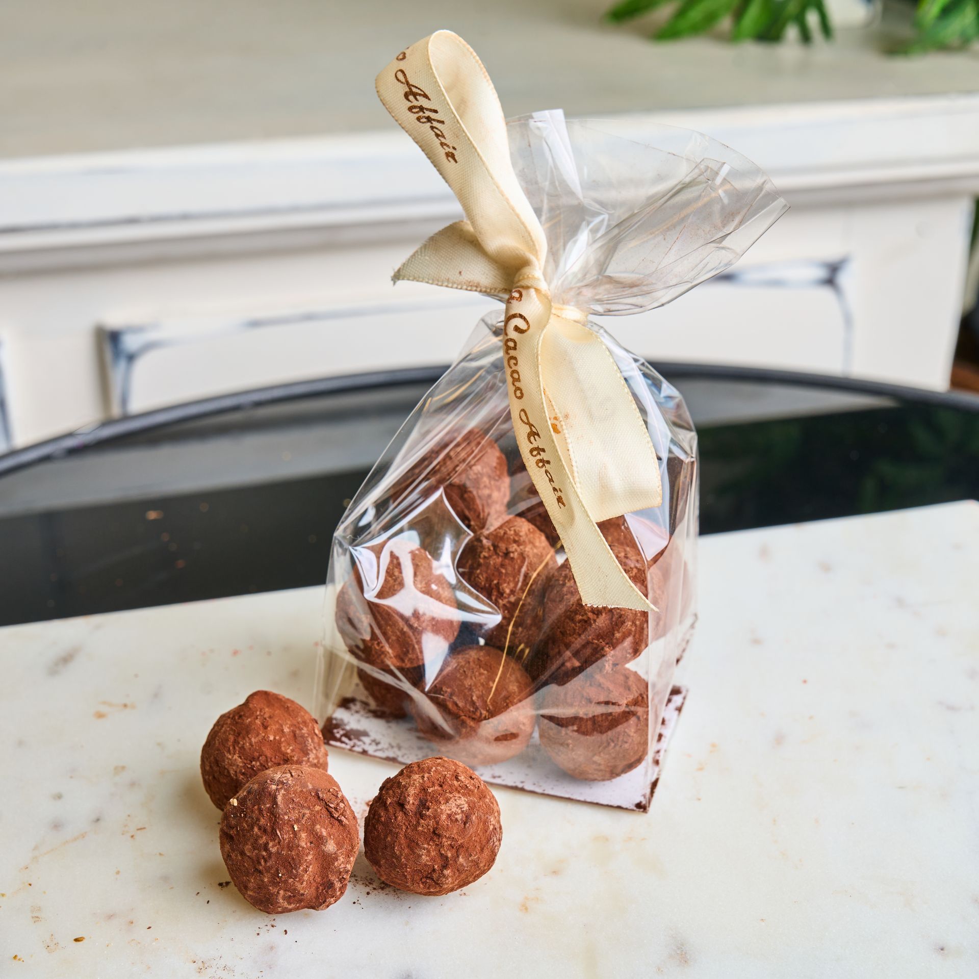 Bag of chocolate truffles tied with a ribbon. Truffles are brown and sit on marble.