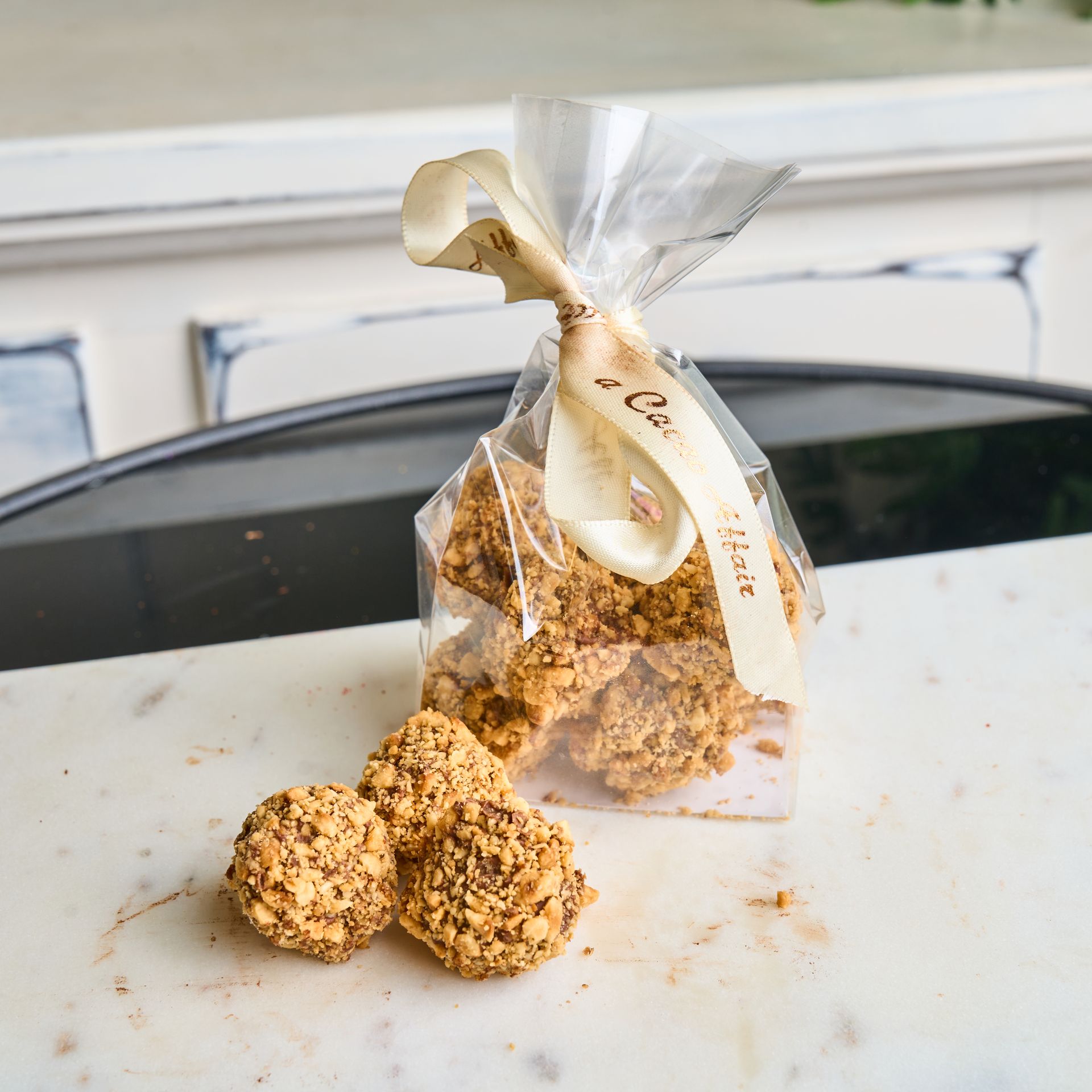Cookies in clear bag with ribbon; three cookies in front. White marble surface.