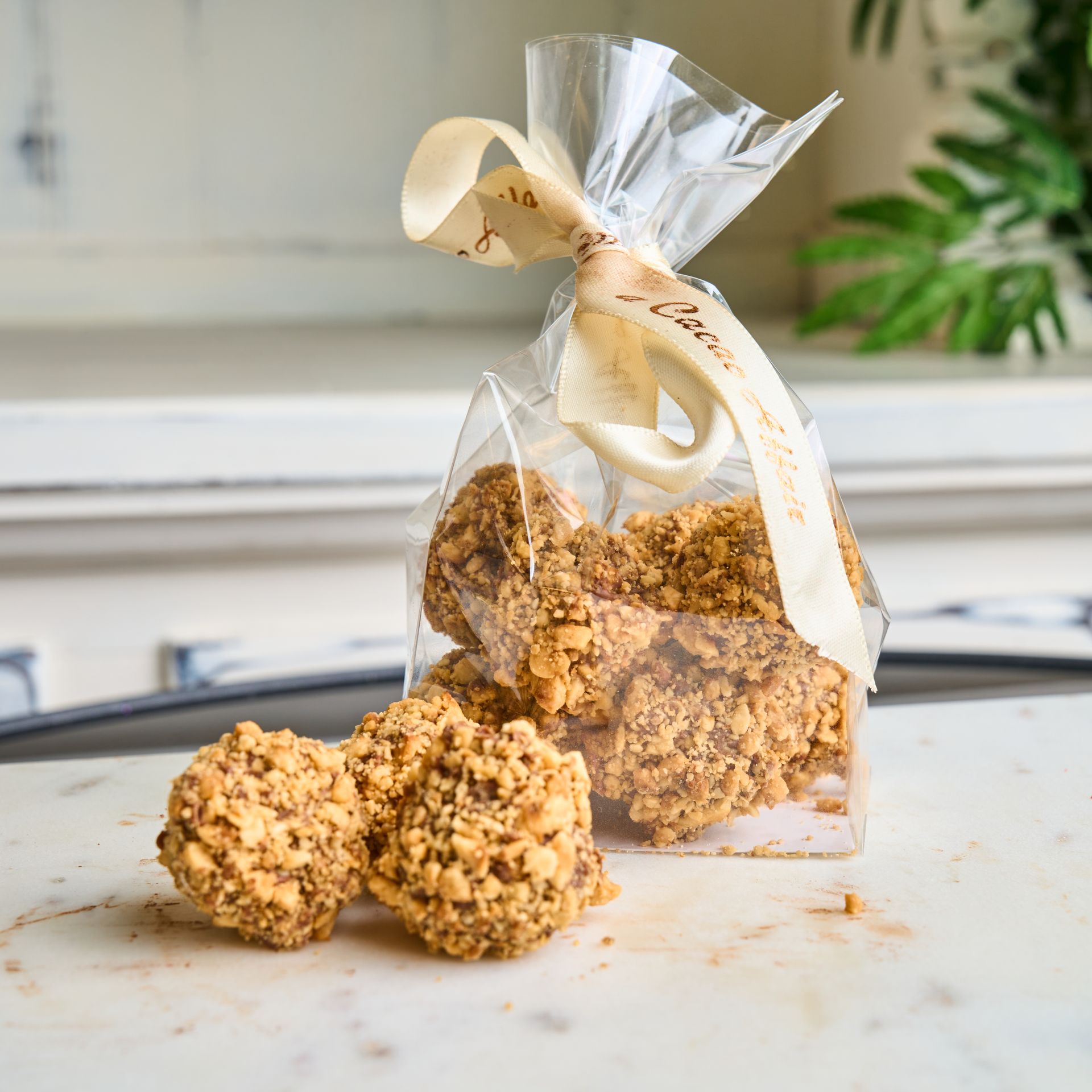 Bag of chocolate candies with nut crumbles, tied with a ribbon, on a marble surface.