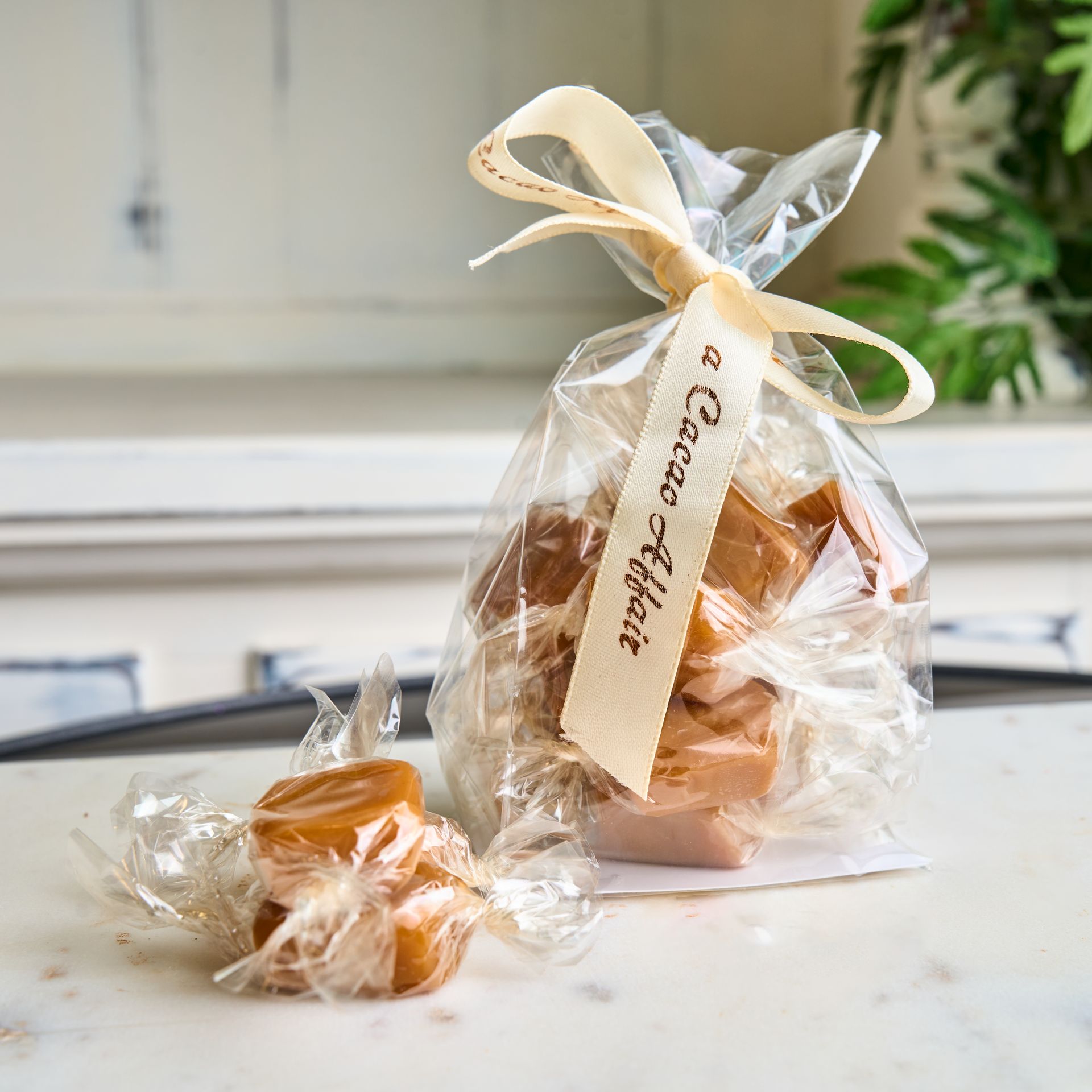 Bag of caramel candies wrapped in clear cellophane and tied with a cream ribbon labeled 