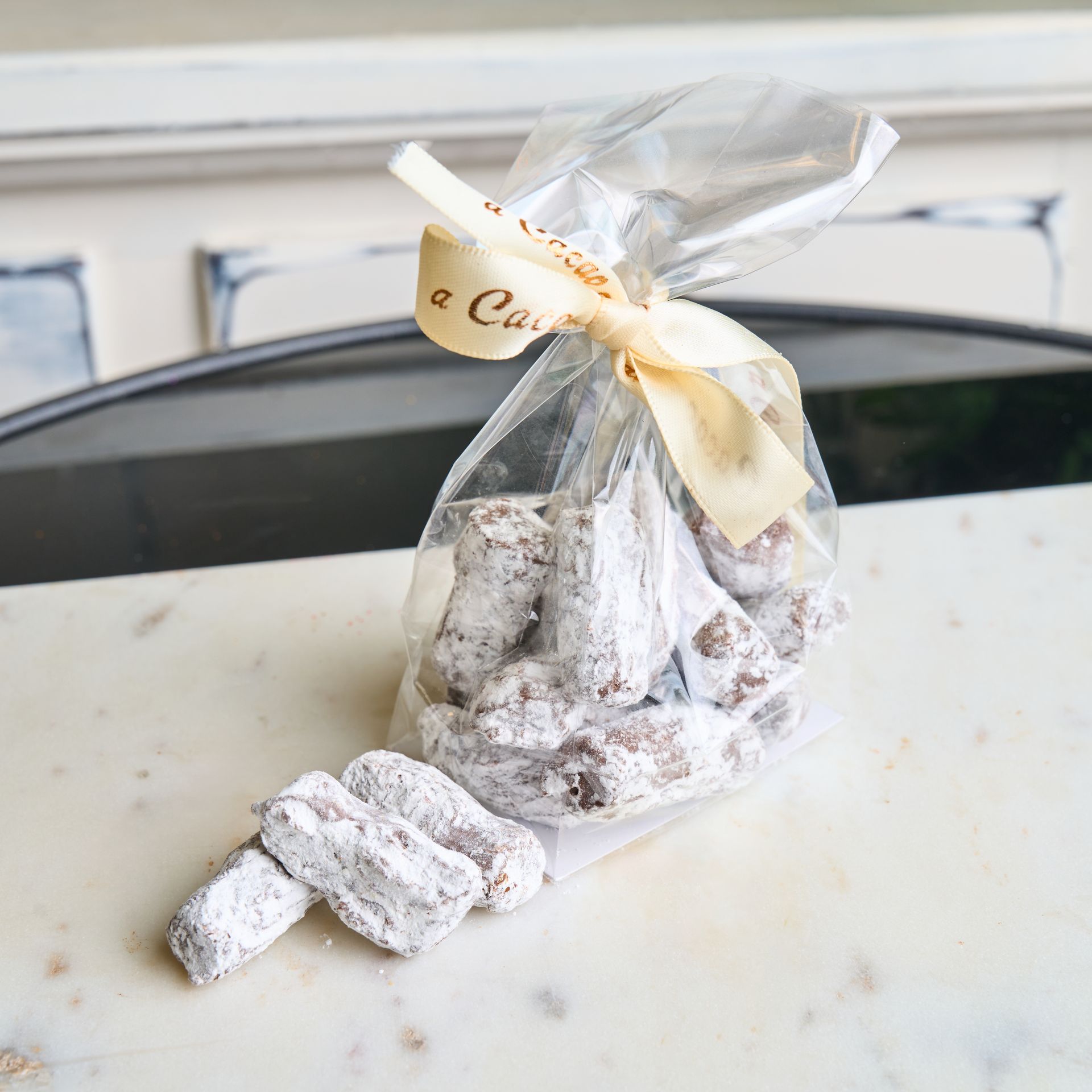 Bag of sugared cookies with ribbon on marble surface.
