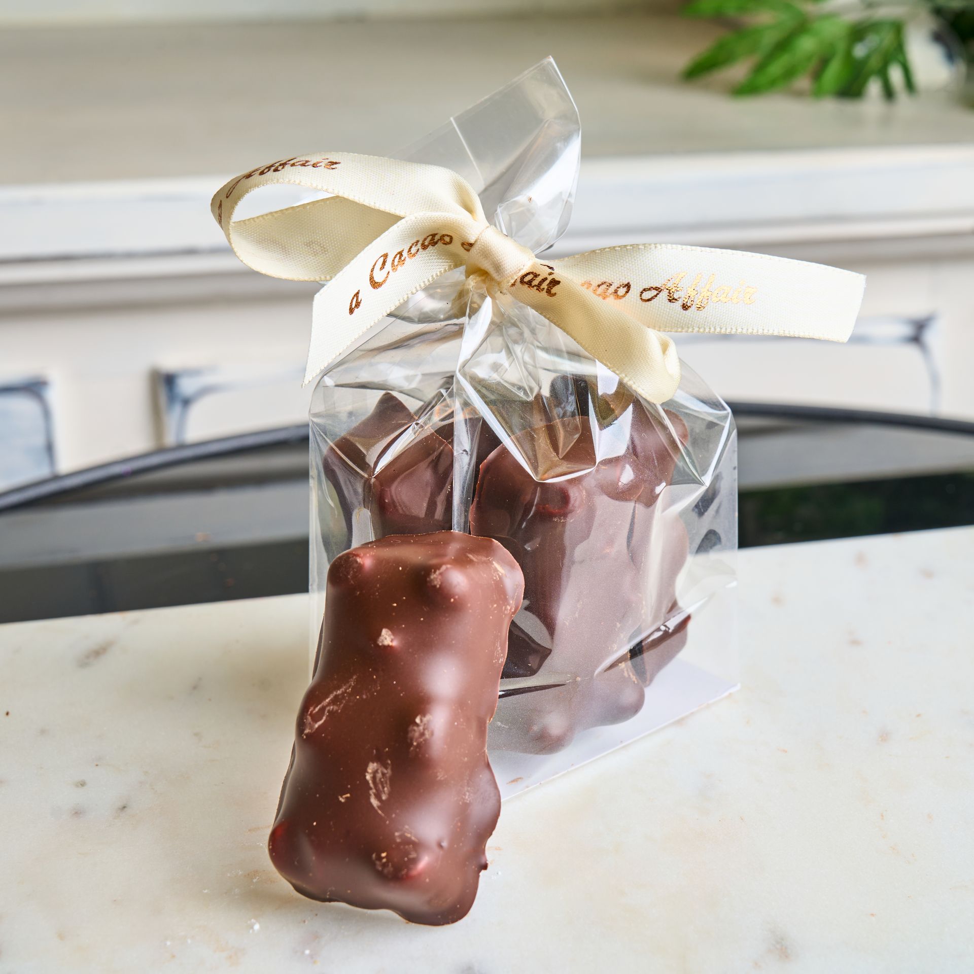 Chocolate candies in a clear bag tied with a ribbon, one candy in front, on a marble surface.