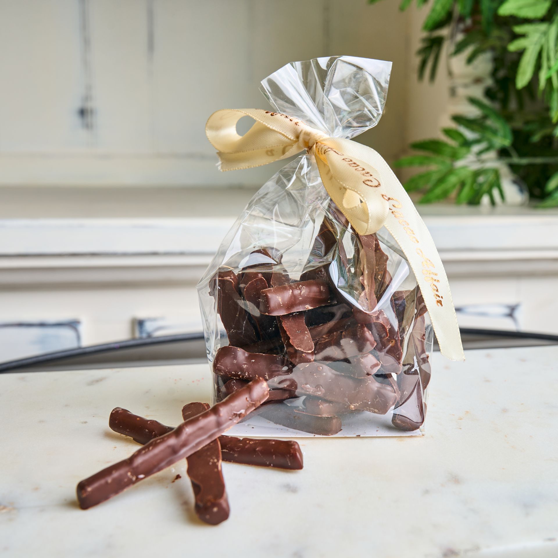 Bag of chocolate-covered pretzel sticks tied with a beige ribbon, sitting on a marble surface.