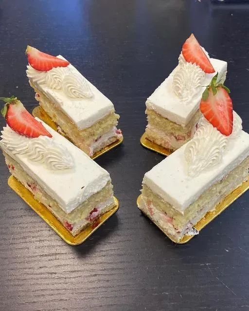 Four strawberry shortcakes with whipped cream and strawberries on a dark surface.