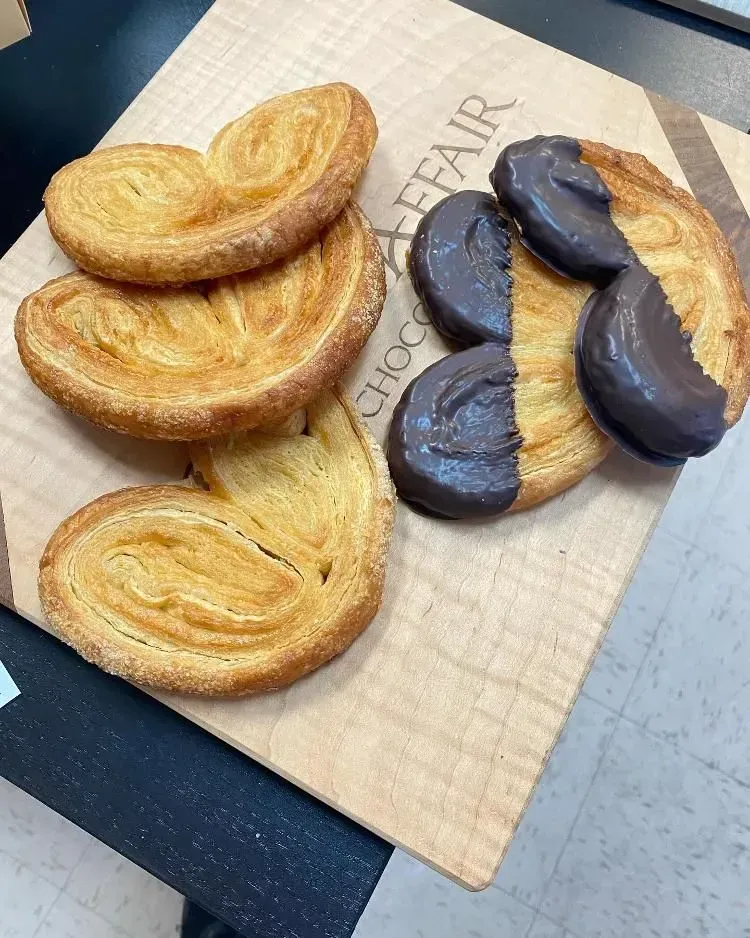 Palmier pastries, some plain, some dipped in chocolate, on a wooden board.