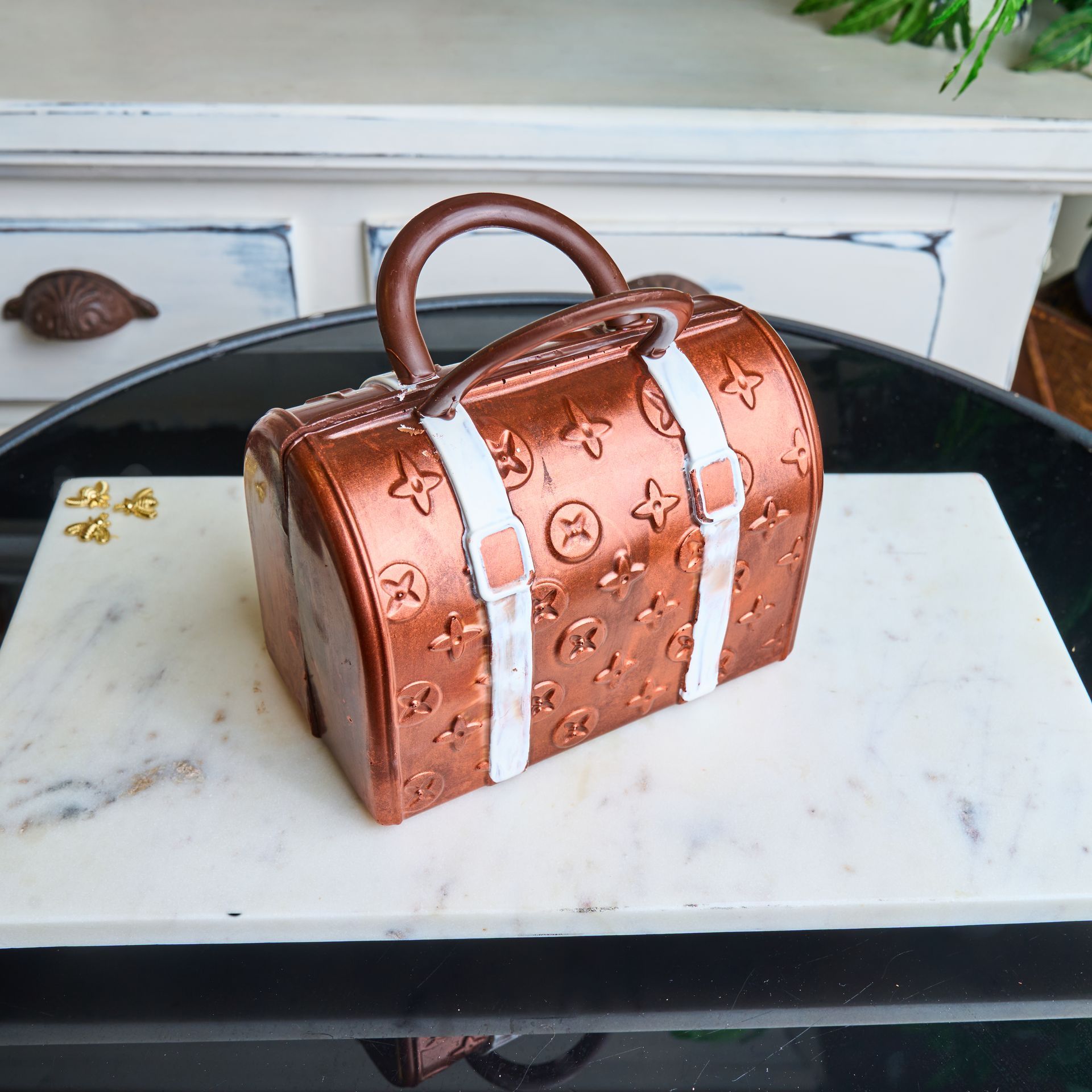 Cake designed as a Louis Vuitton handbag, brown with white straps, on a marble slab.