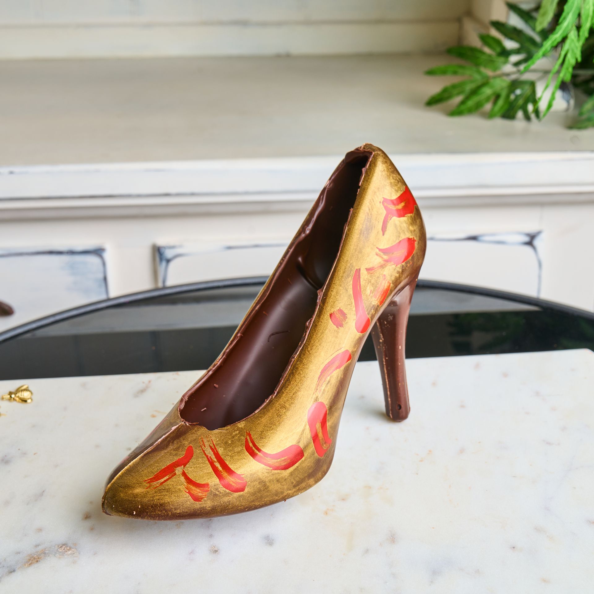 Chocolate high heel with gold and red accents on a marble surface.