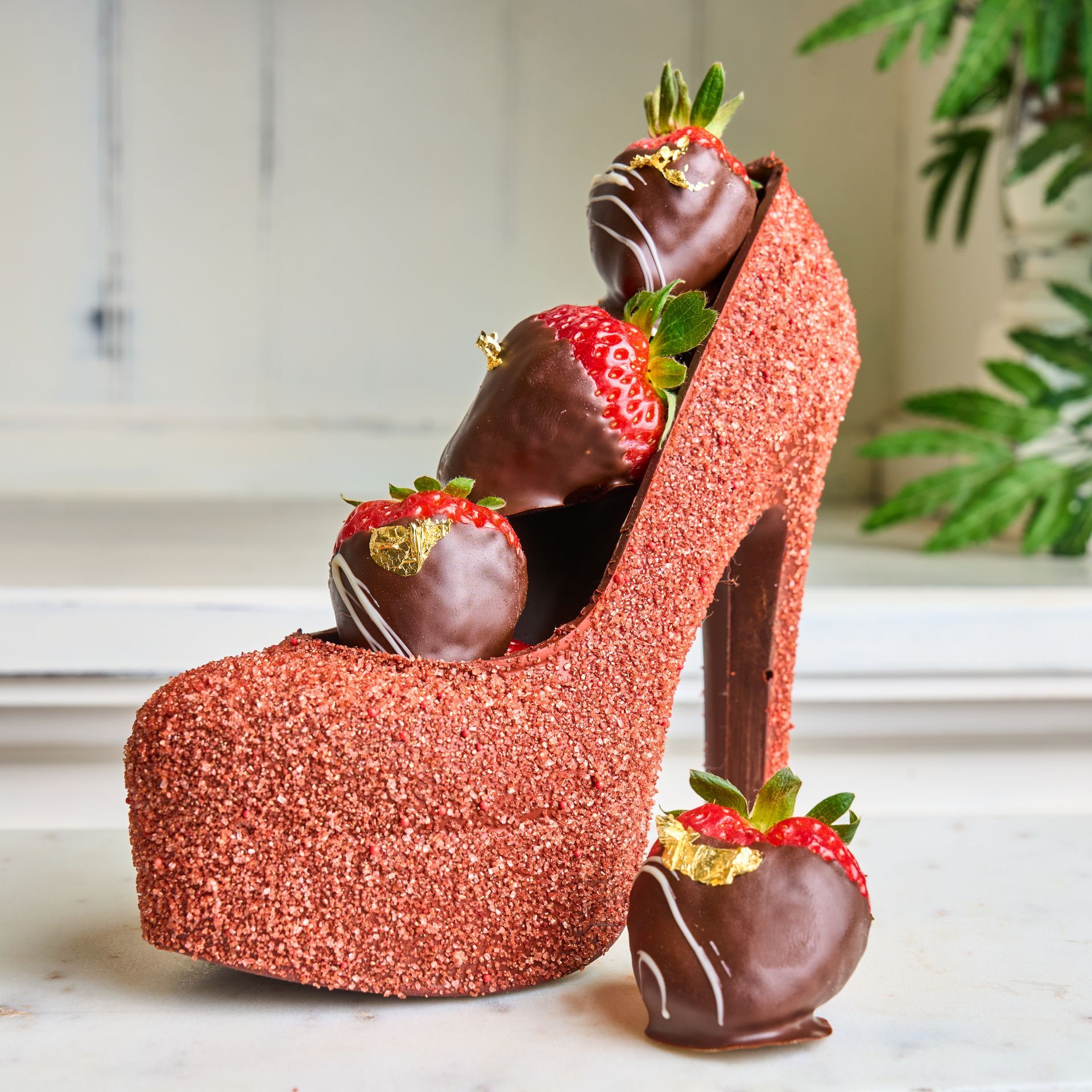 Chocolate shoe sculpture with chocolate-covered strawberries, some with gold leaf accents.
