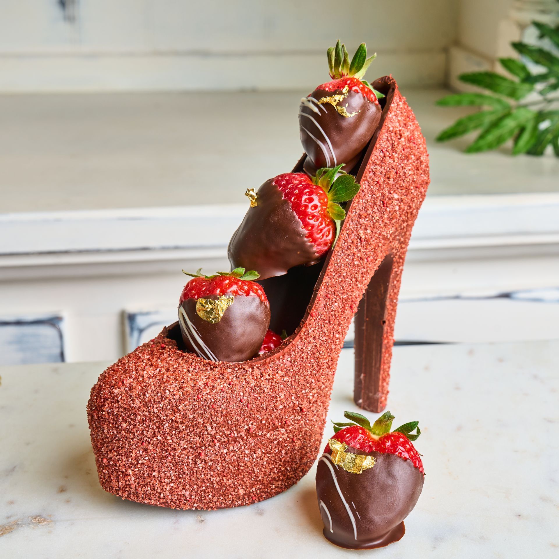 Chocolate-covered strawberries in a sparkly pink high-heeled shoe, with one strawberry beside it.
