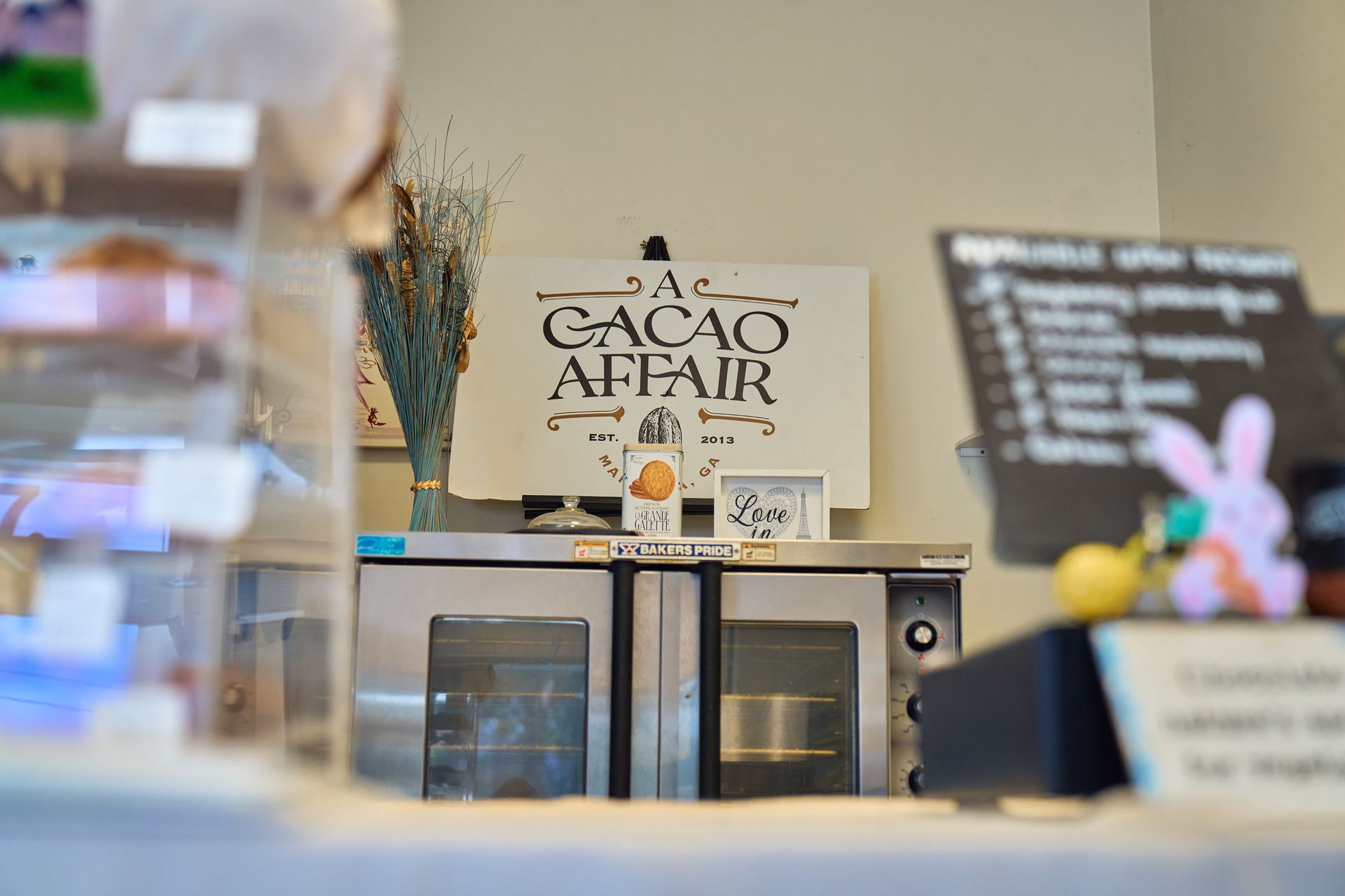 A Cacao Affair sign above a commercial oven, with pastries in a display case on the left.