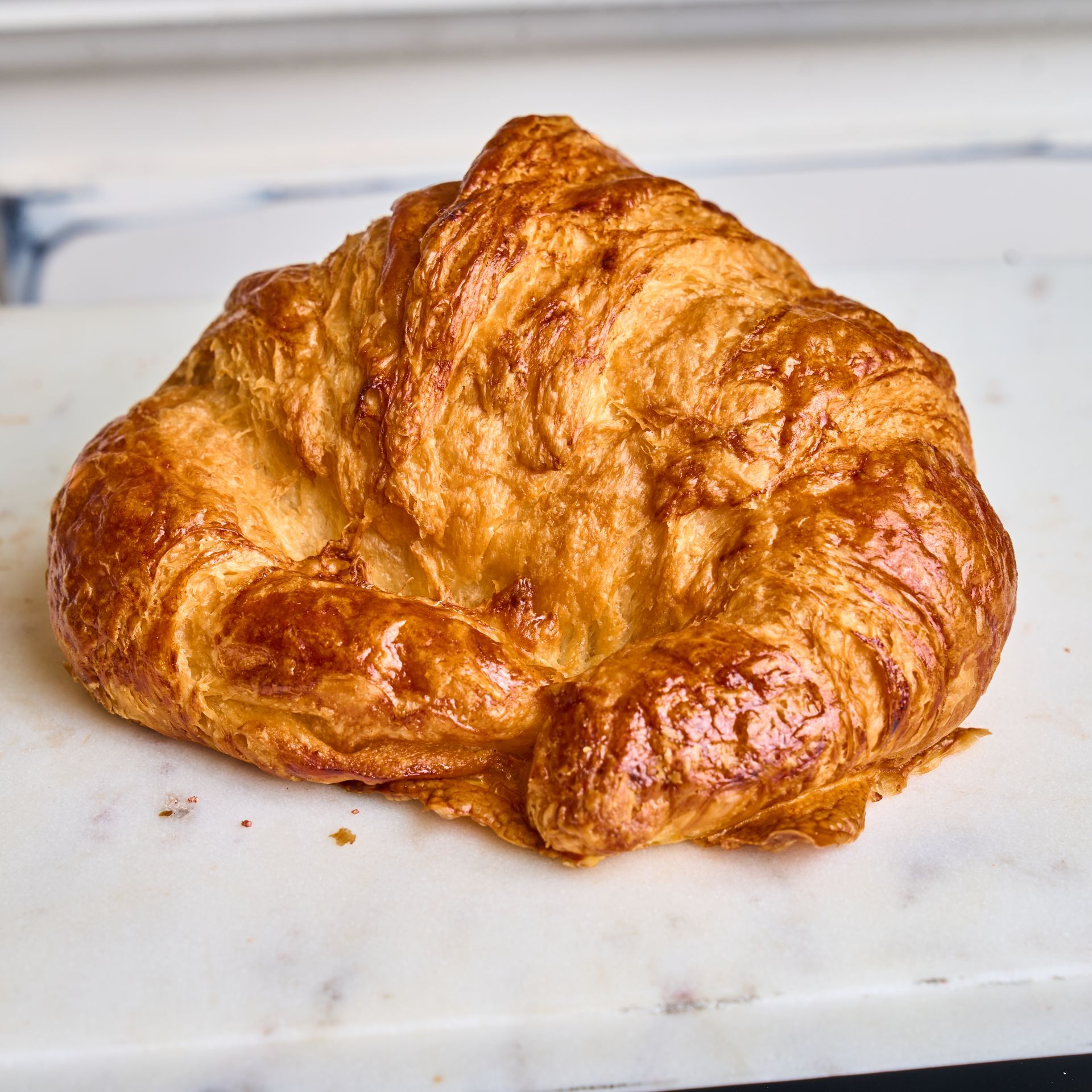 Golden, flaky croissant on a white marble surface.