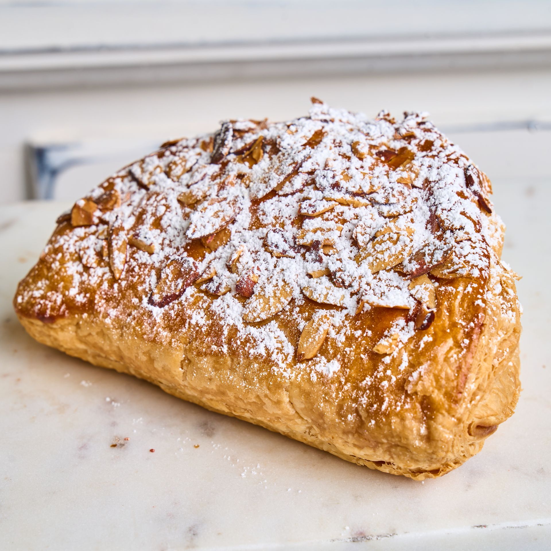 Almond croissant dusted with powdered sugar and almond slivers, on a marble surface.