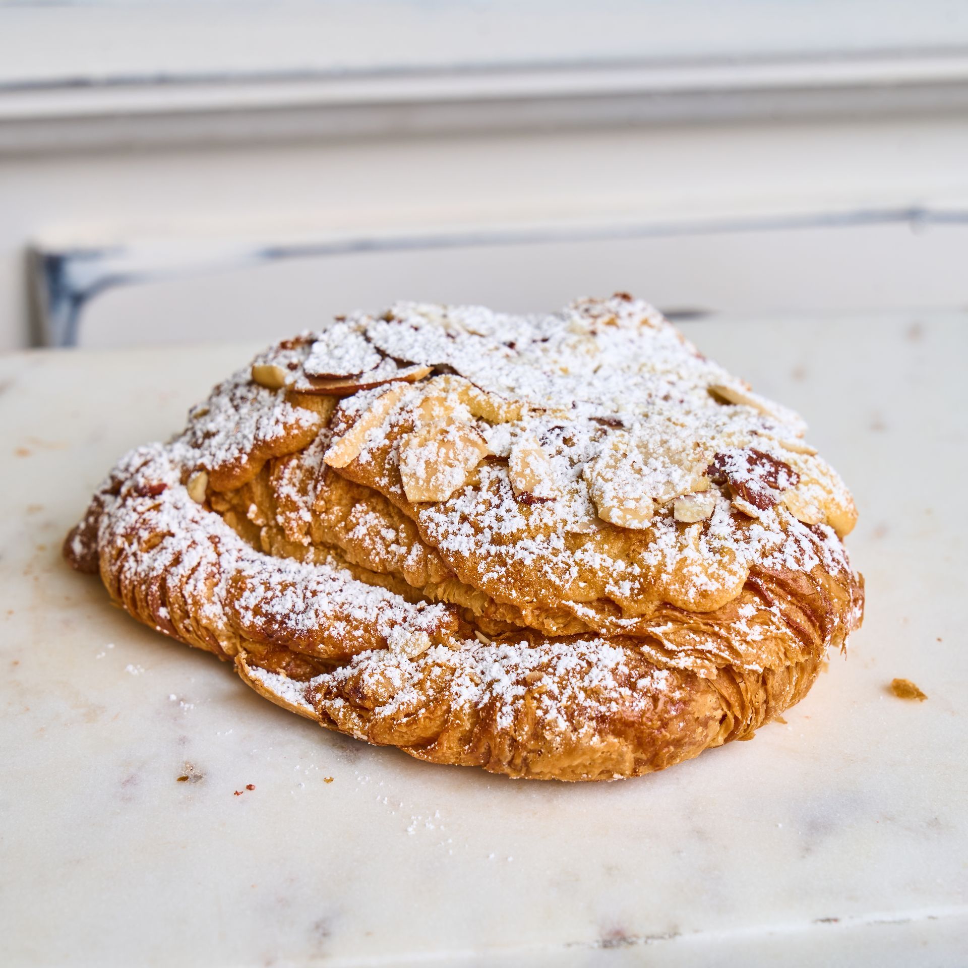 Almond croissant dusted with powdered sugar and almond slivers, on a marble surface.