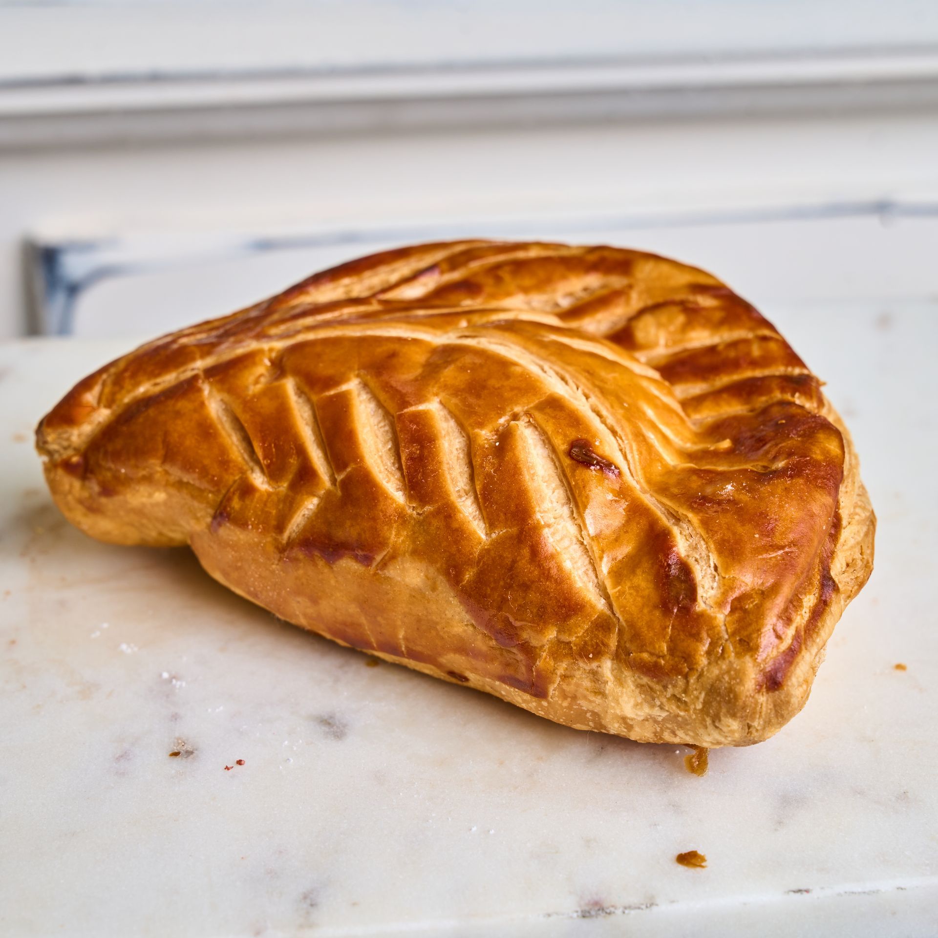 Golden, baked pastry on a marble surface, with leaf-like scored pattern.