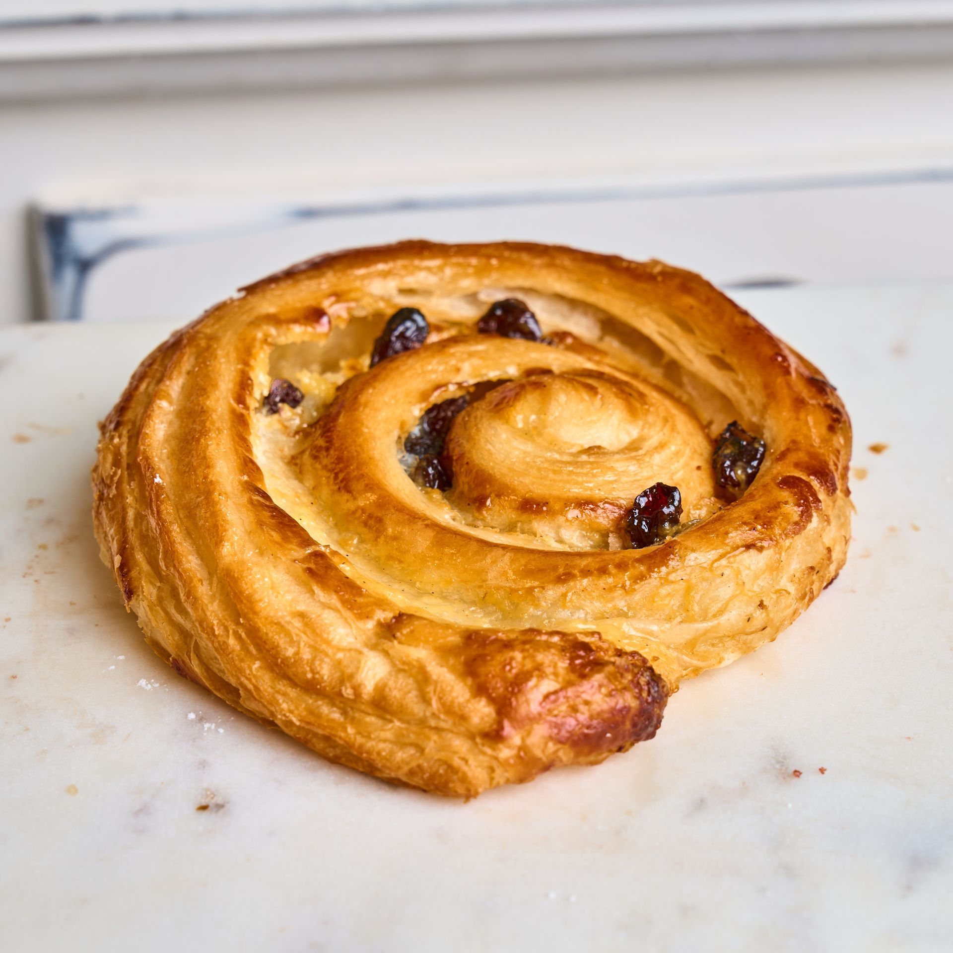 A golden, spiral-shaped pastry with raisins on a marble surface.