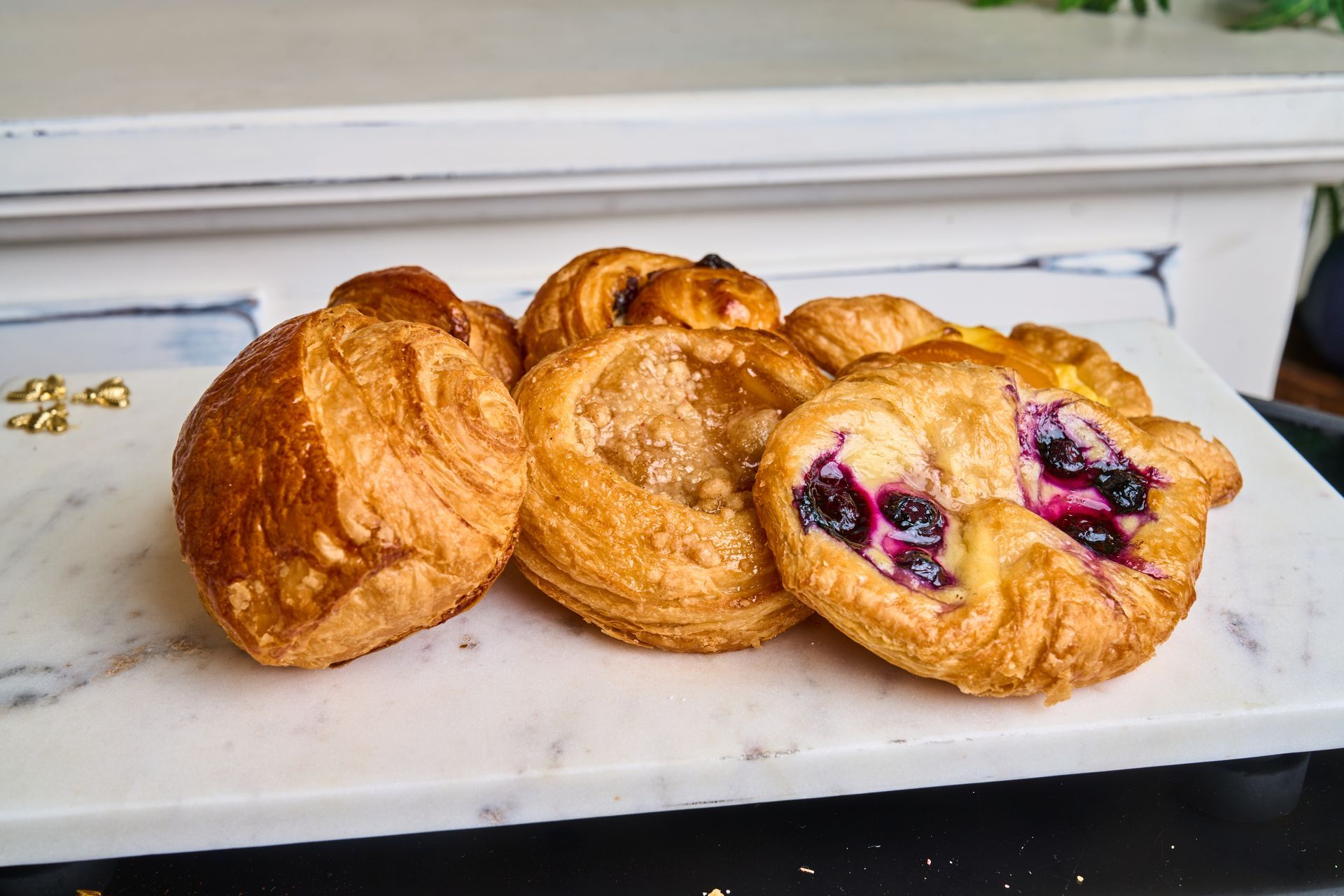 Assortment of golden-brown pastries on a white marble slab; one filled with blueberries.