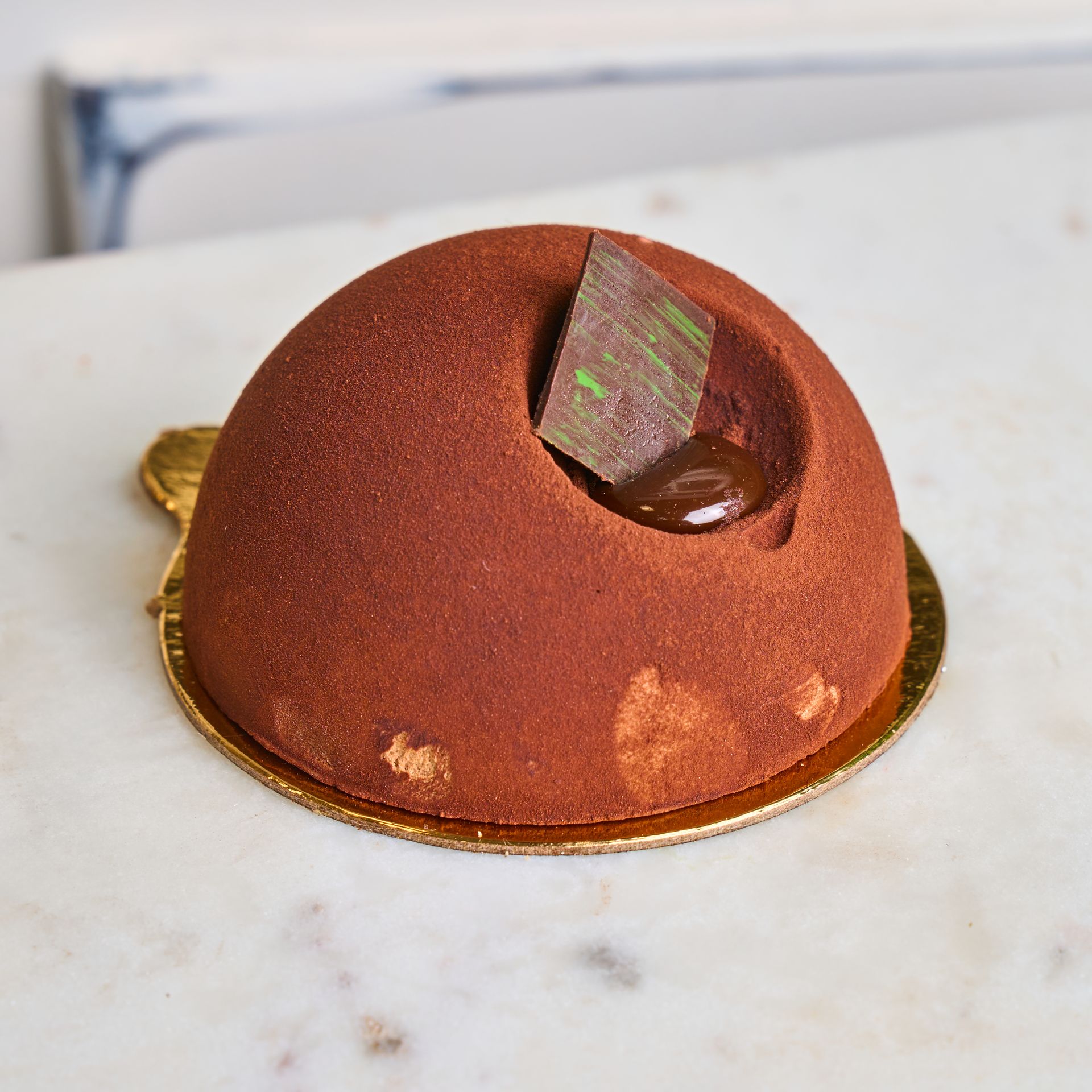 Chocolate dome cake with a square chocolate decoration. On a gold cake board.