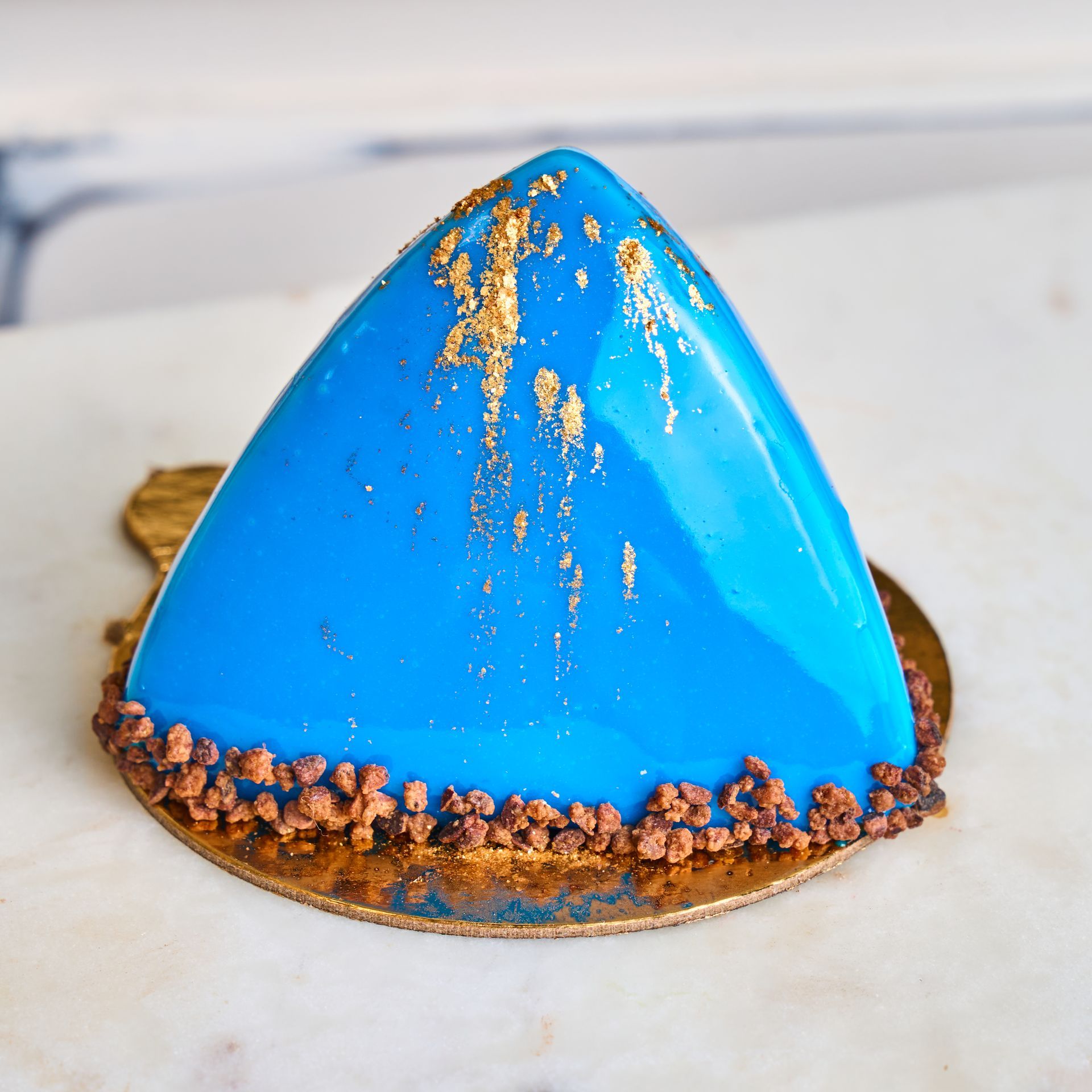Blue, triangular-shaped dessert with gold accents on a gold base, with a chocolate border.