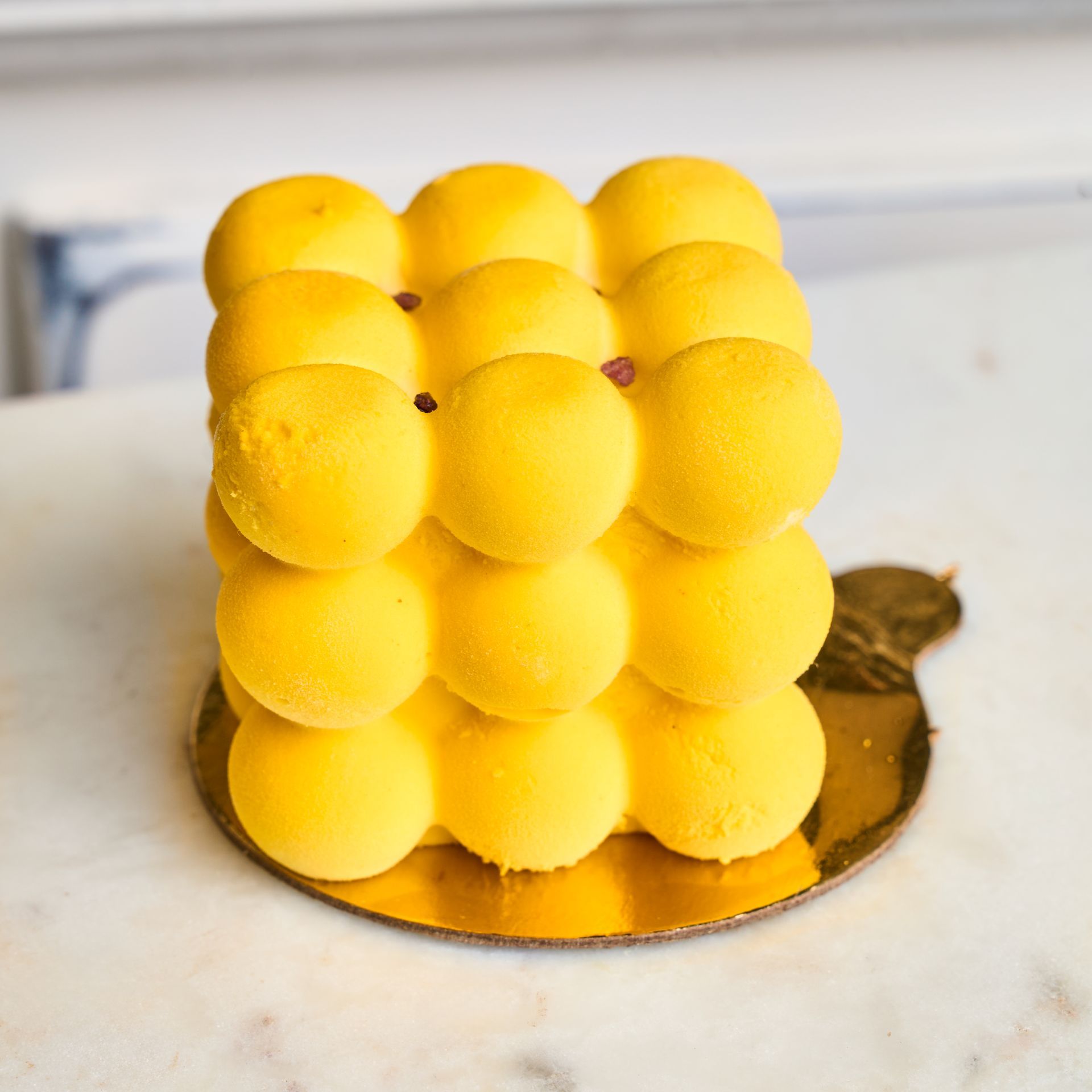 Yellow cube-shaped cake with spherical components on a golden base.