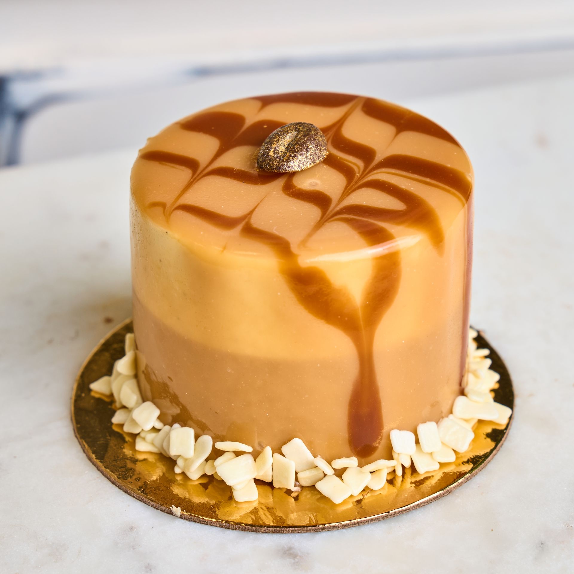 Caramel cake with caramel drizzle and gold flakes, on a gold base with white almond slivers.