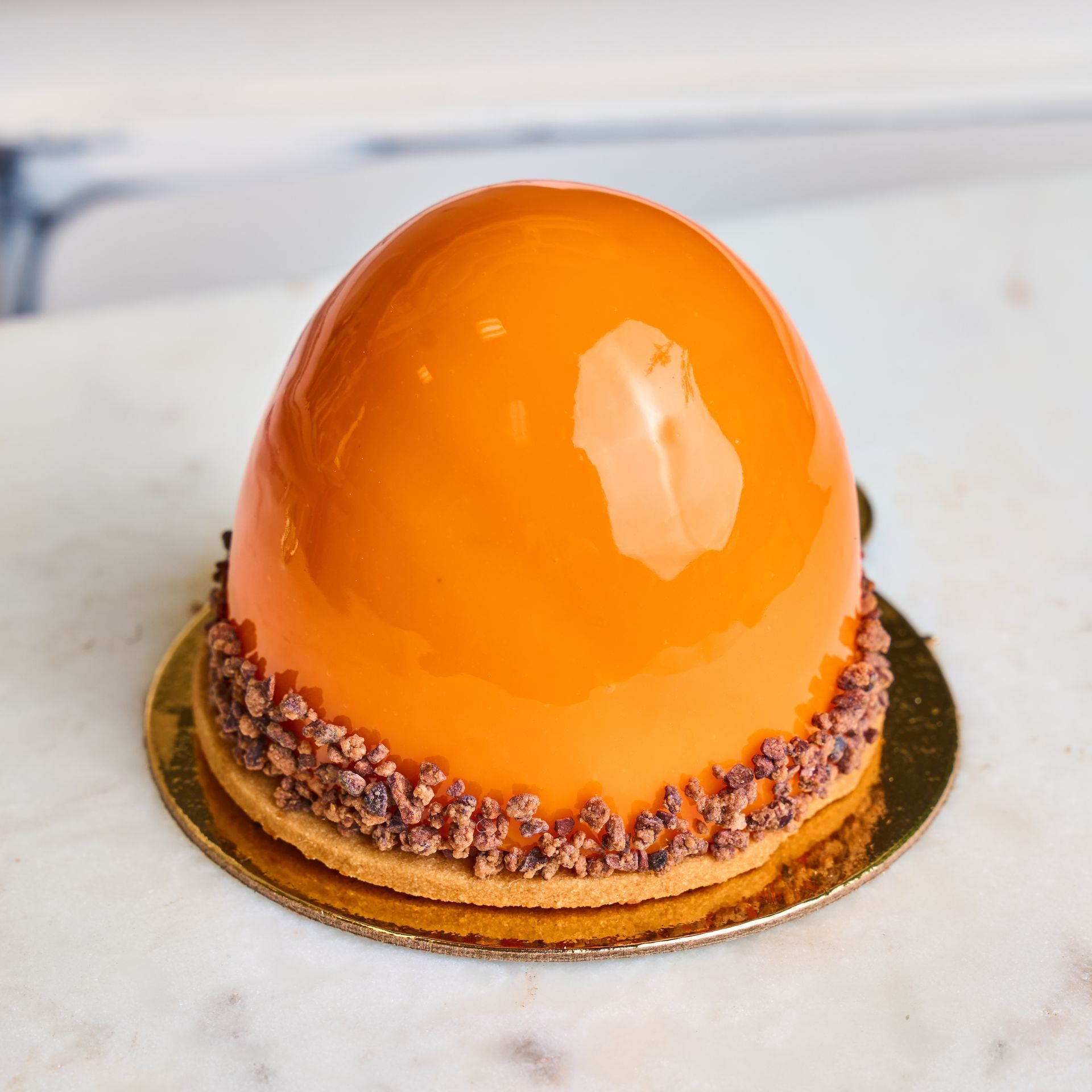 Orange glazed dome cake with chocolate crumble on a gold base.