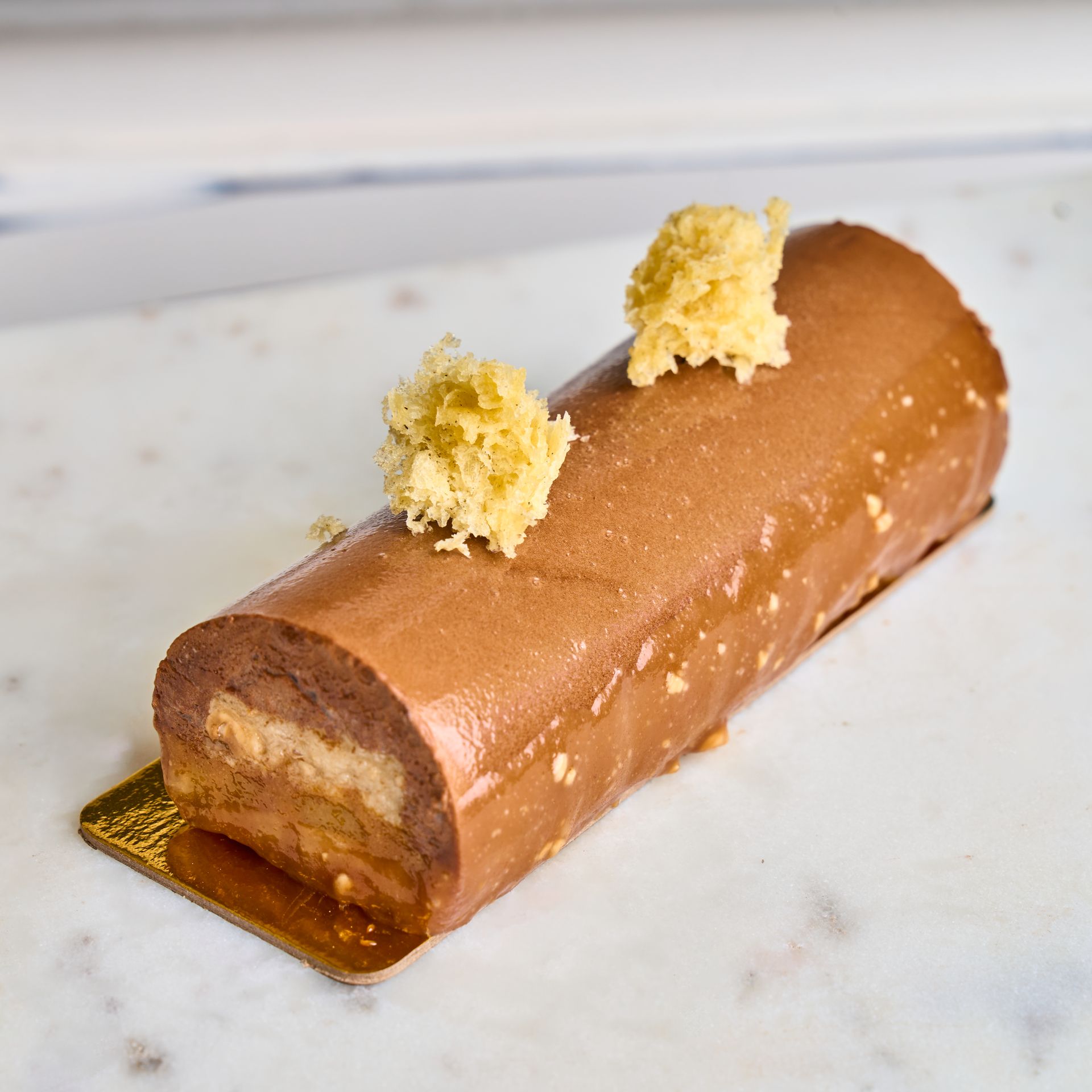 Chocolate log cake with yellow crumble topping on a gold plate.