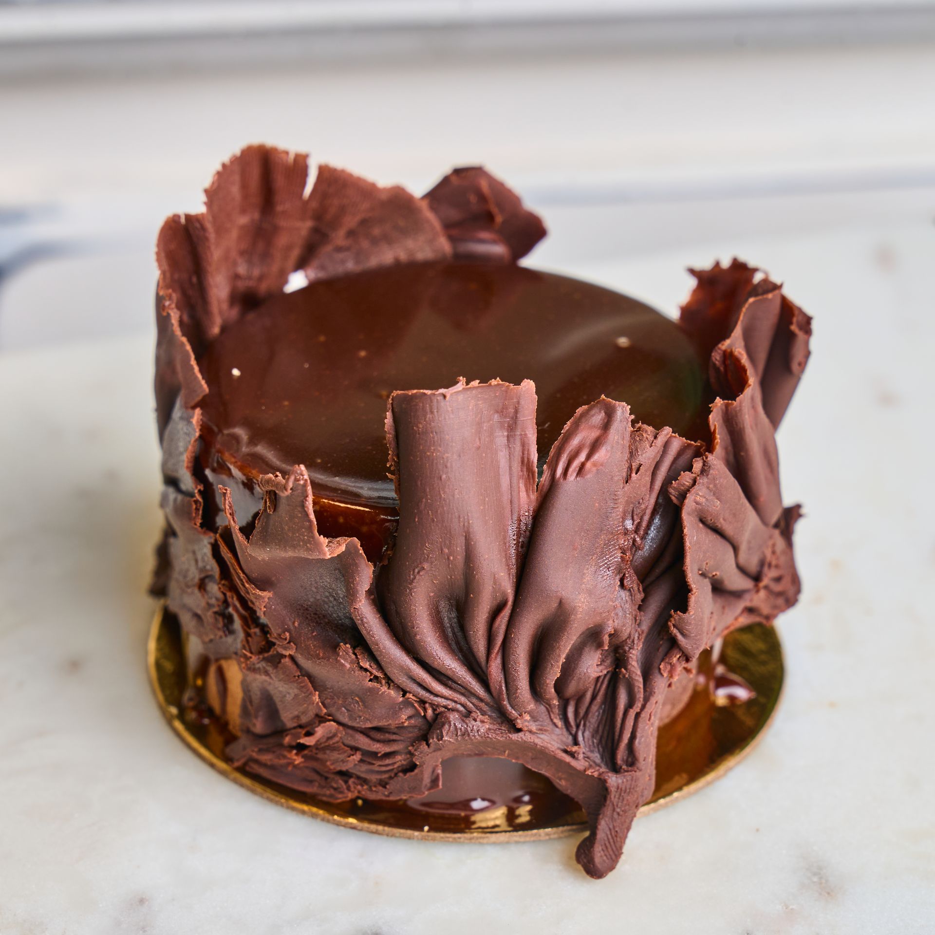 Chocolate cake with dark glaze and chocolate embellishments on a gold base.