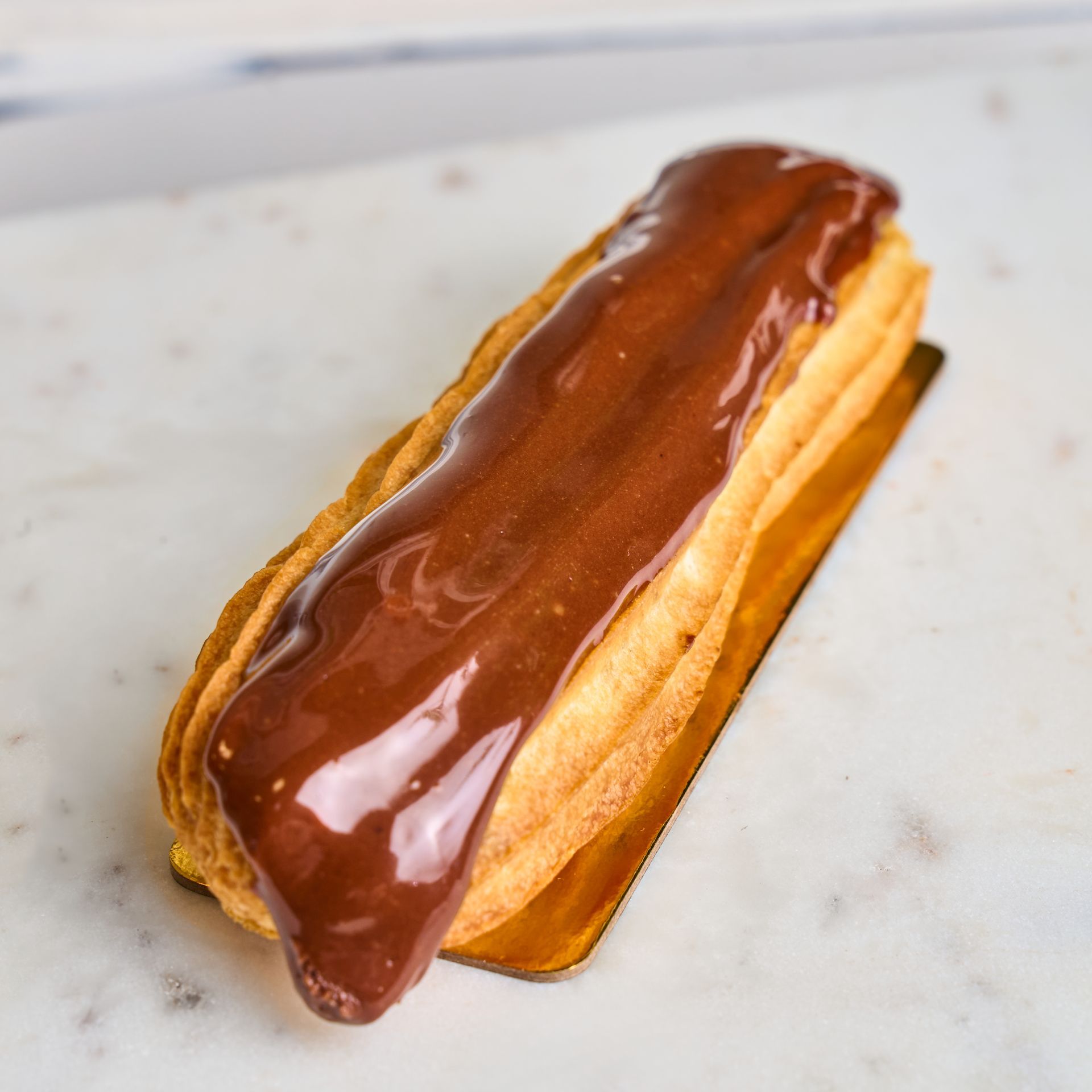 Chocolate éclair on a gold tray, with a glossy chocolate topping and cream filling.