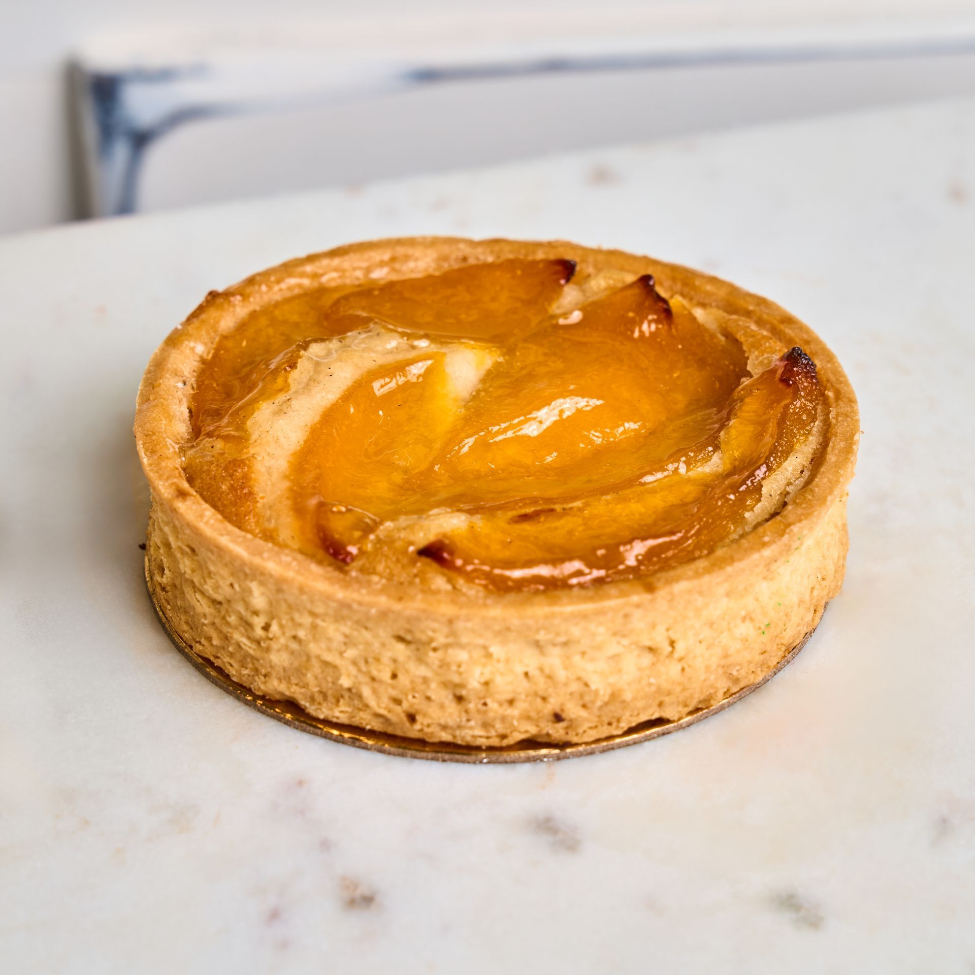 Peach tart on a white marble surface, golden crust and peach slices.
