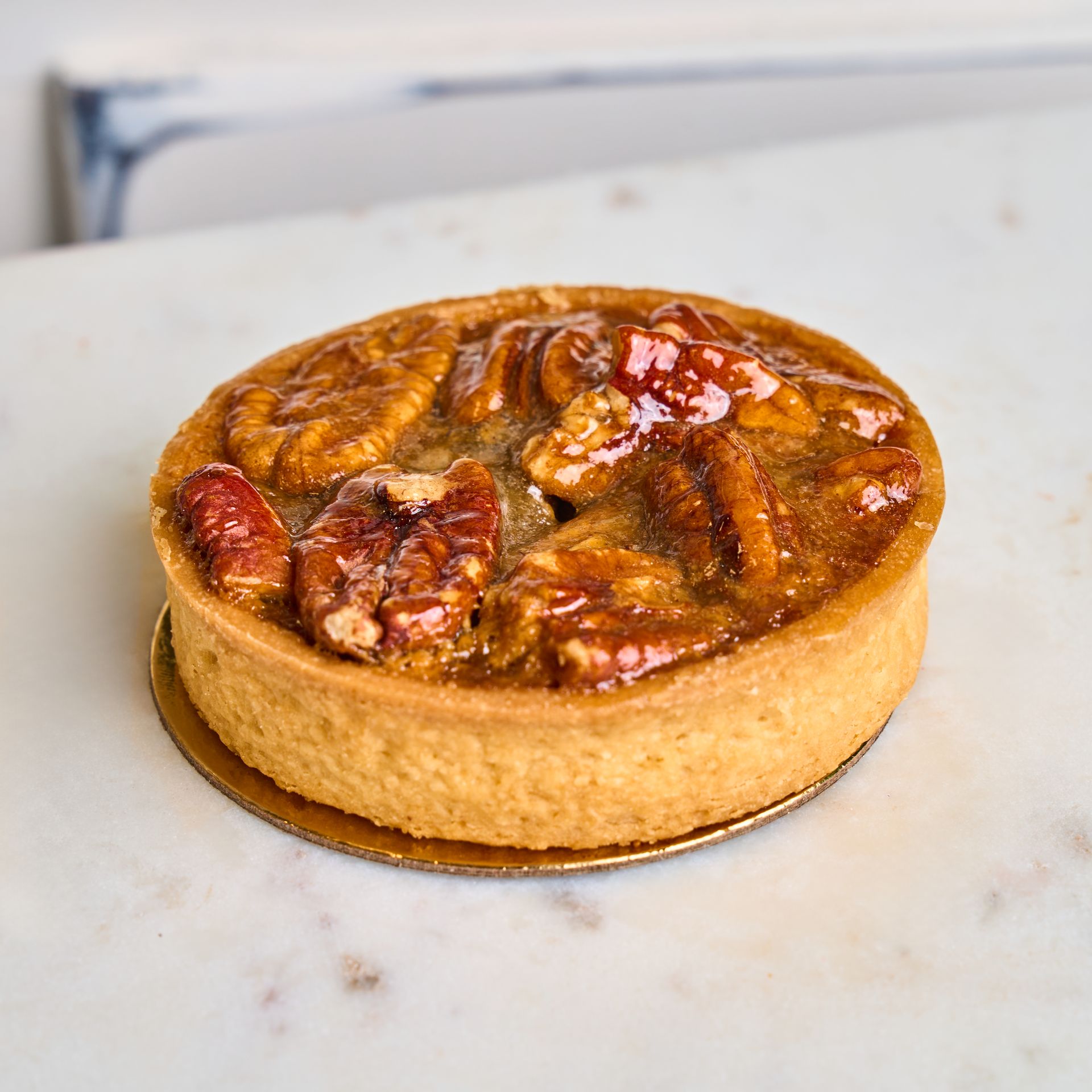 Pecan tart on a marble surface. The filling is glossy, and the crust is golden brown.
