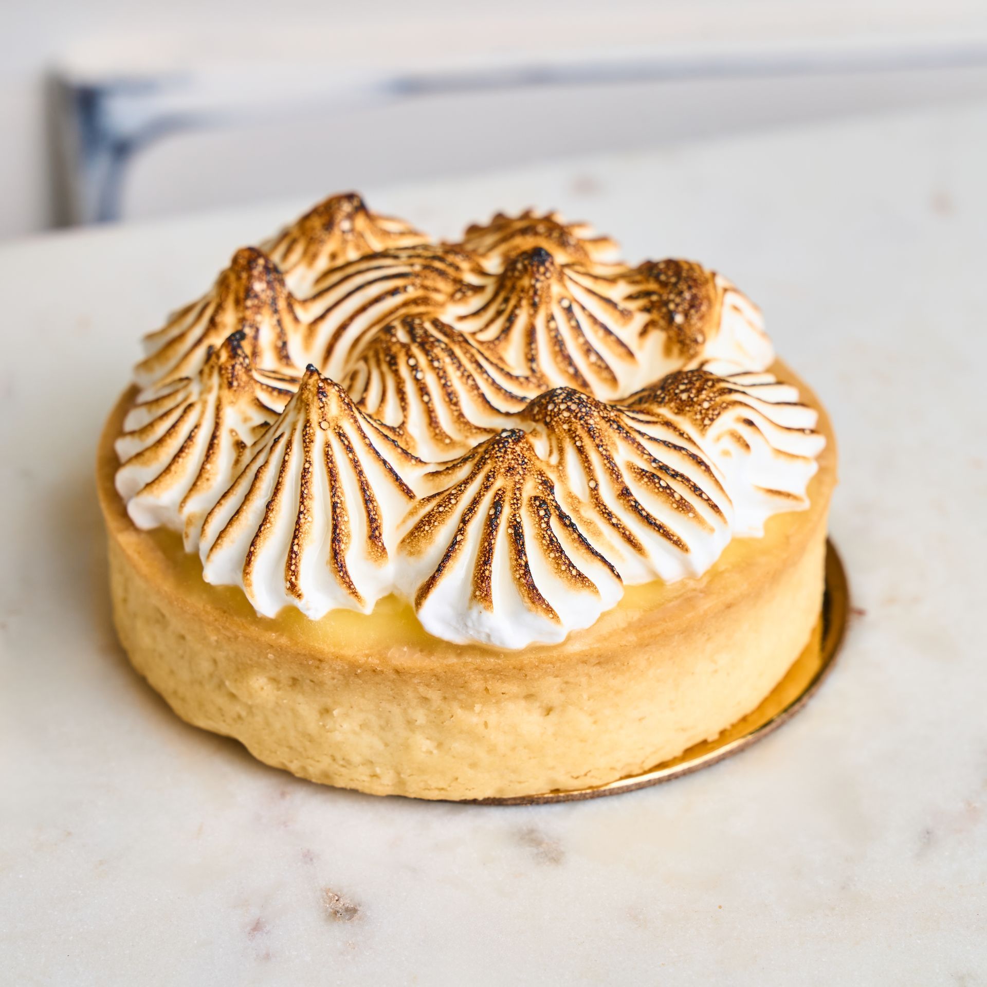 Lemon meringue tart on a white marble surface, topped with toasted meringue.