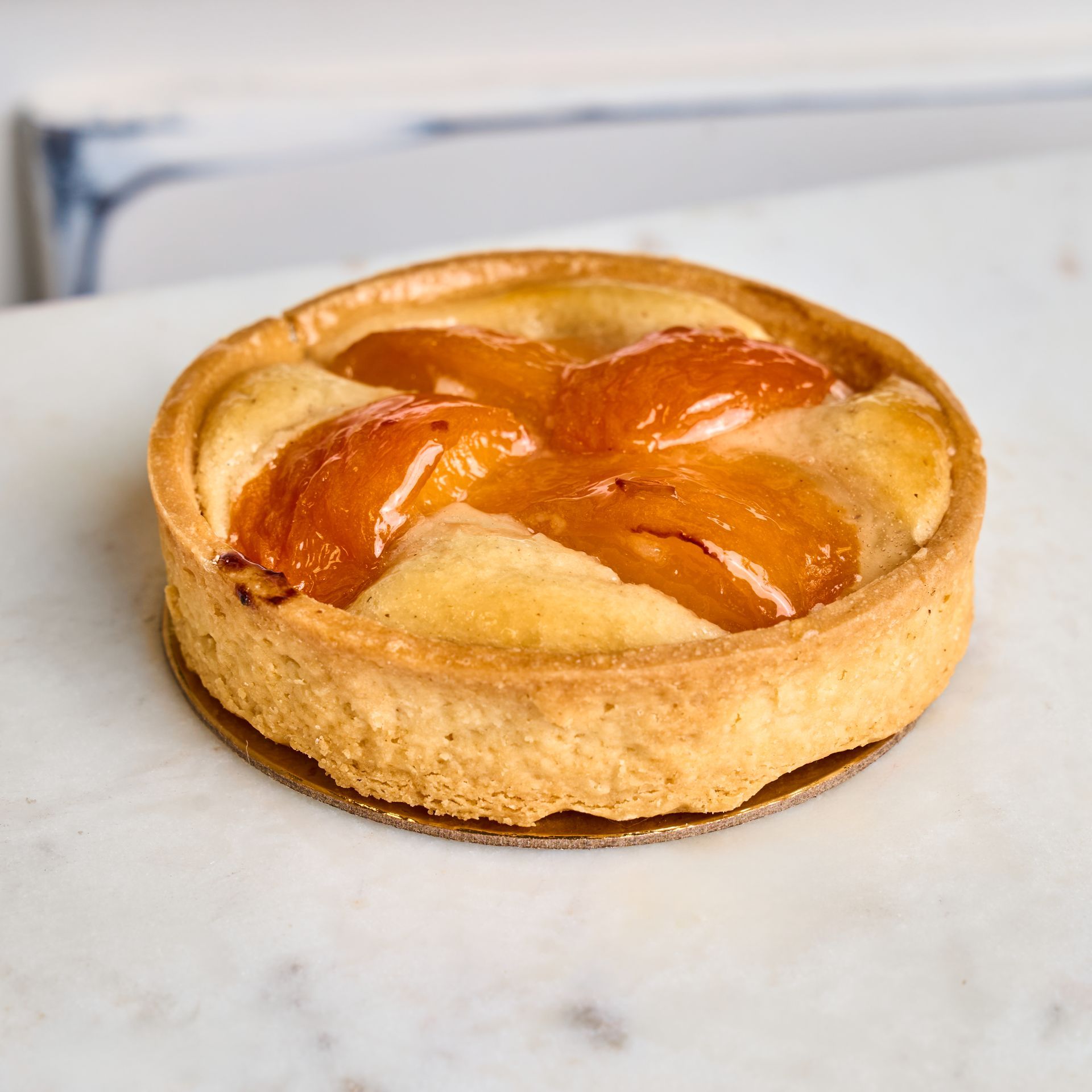 Peach tart on a marble surface, golden crust with glazed peach slices.