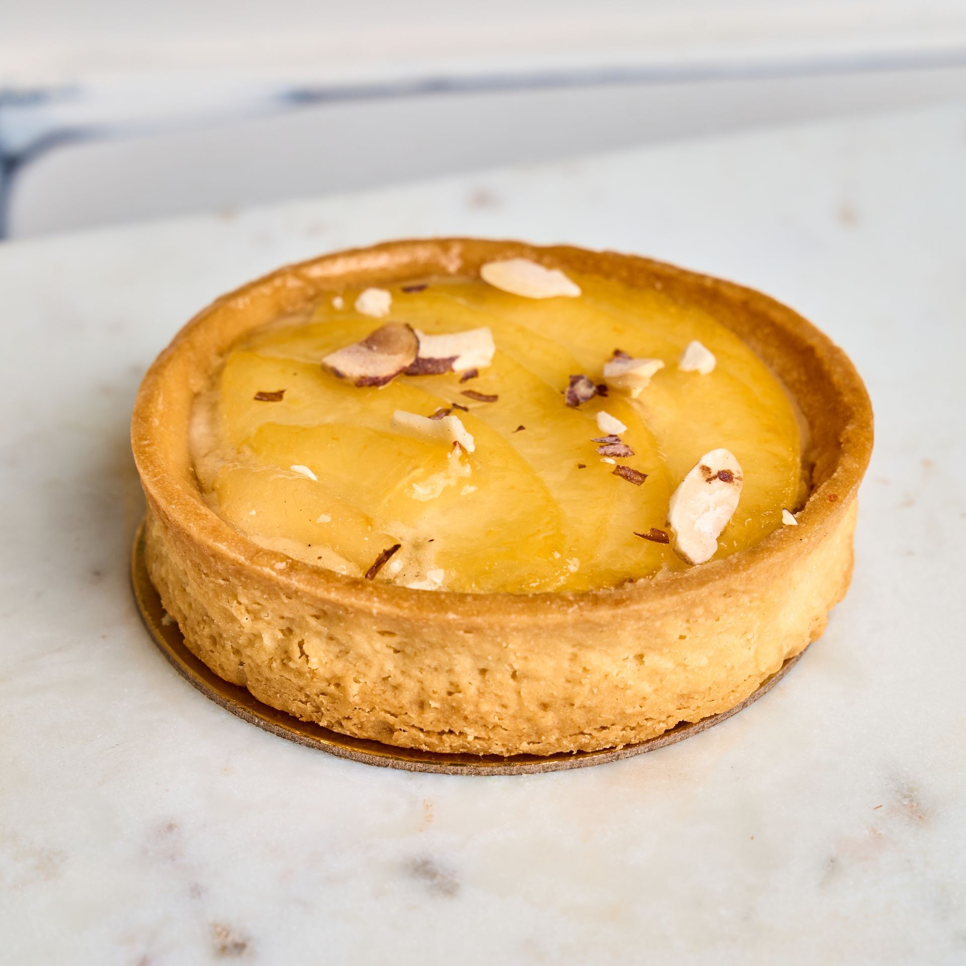 Round fruit tart with a flaky crust, topped with sliced fruit and nuts, on a marble surface.