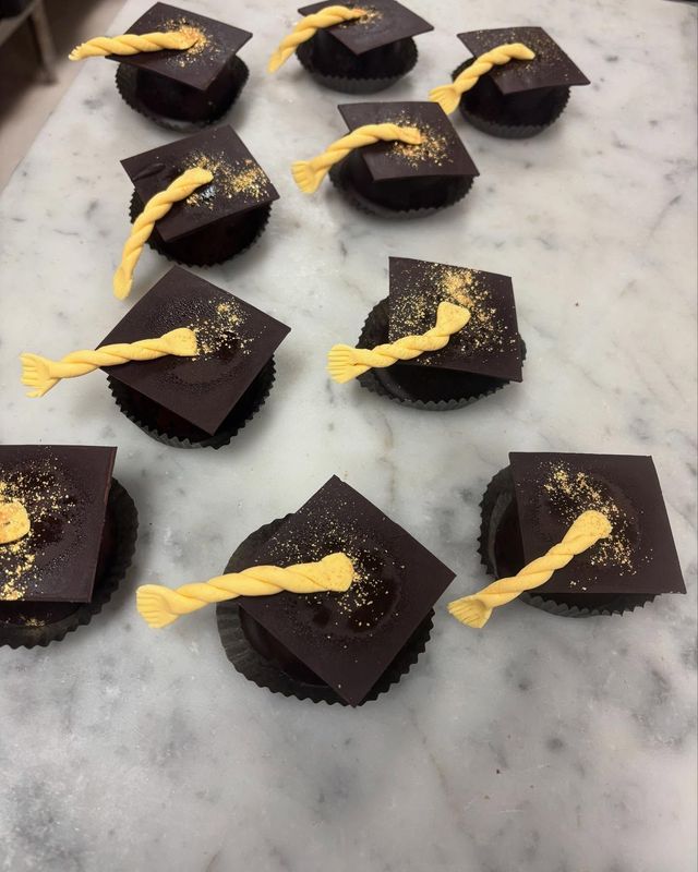 Chocolate graduation cupcakes on a marble surface, topped with yellow tassels and gold sprinkles.