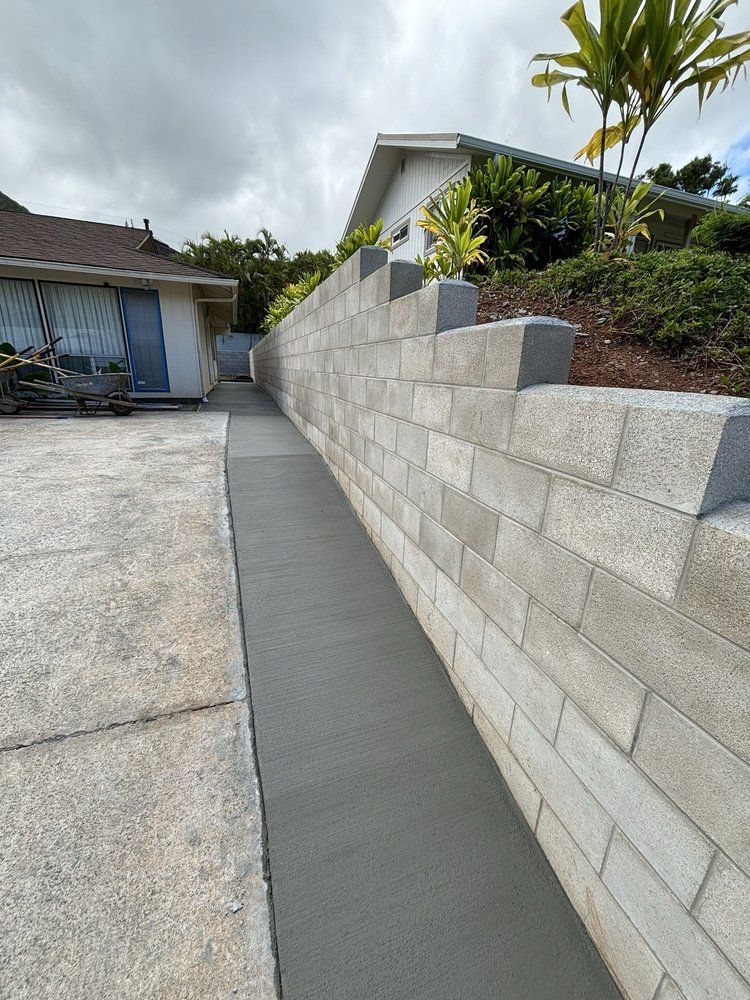 A concrete walkway leading to a house next to a brick wall