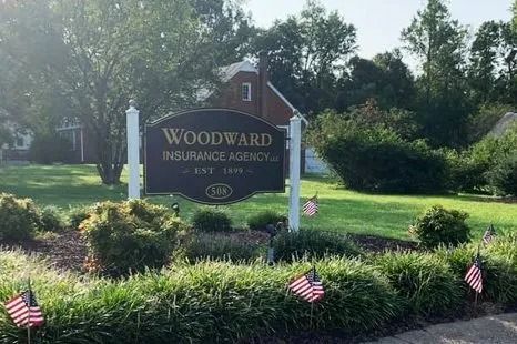 Woodward Insurance Agency sign in a landscaped yard with small American flags and trees behind it