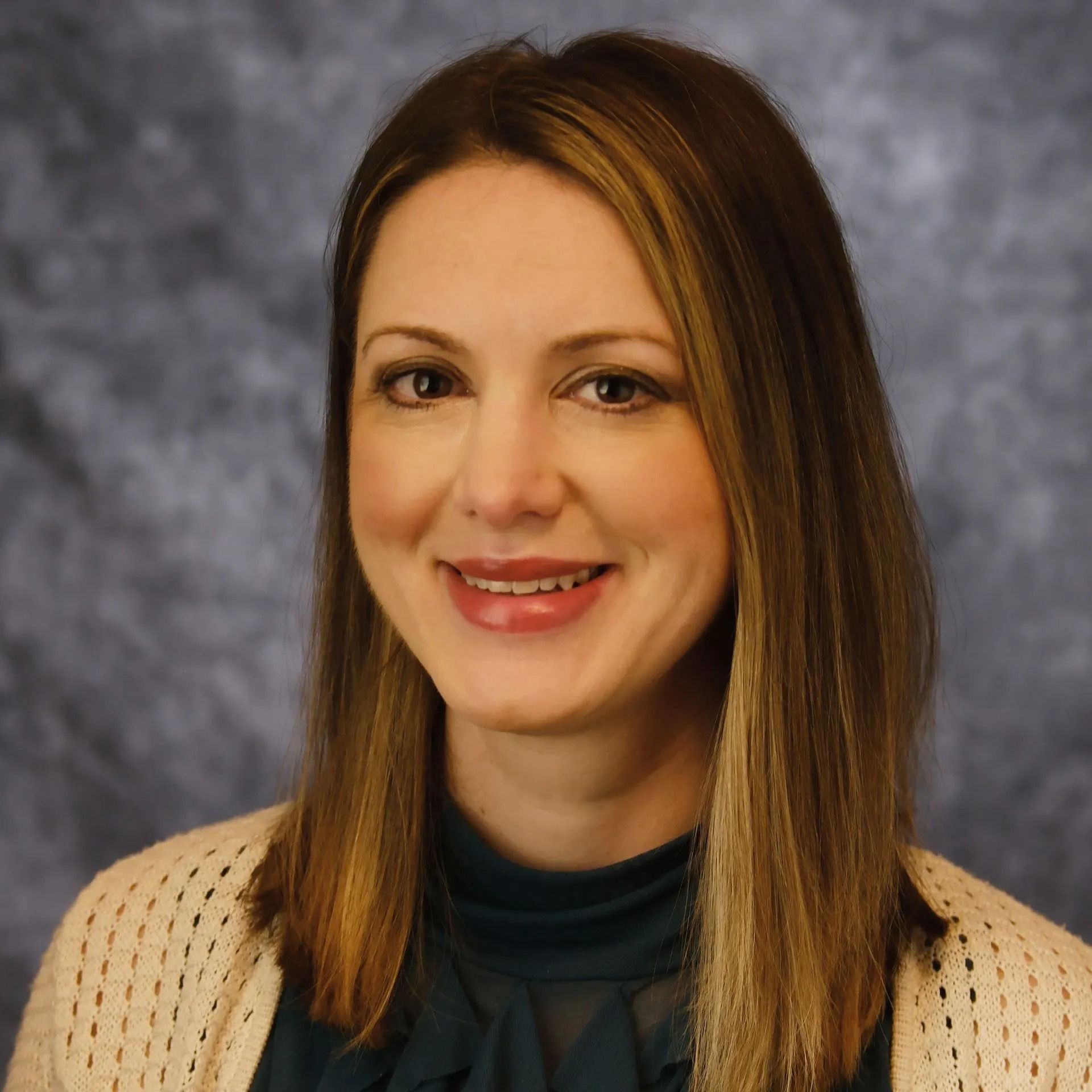 Portrait of a smiling woman with straight brown hair against a gray studio backdrop