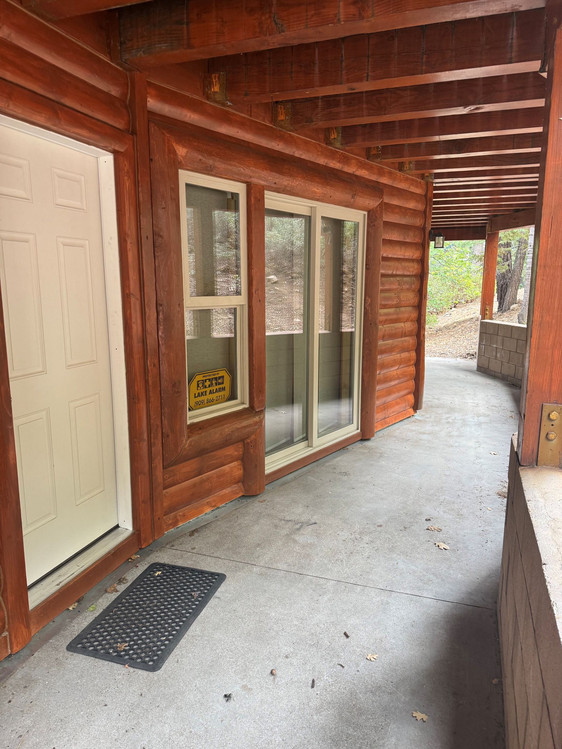Exterior of a cabin with a curved concrete walkway, white door, and windows under a wooden overhang.