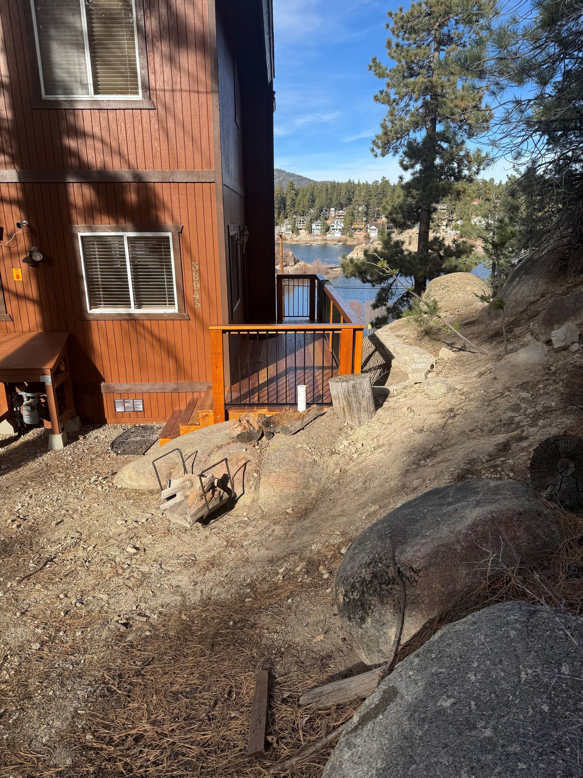 Brown house with small deck overlooking a lake, nestled in a rocky hillside with trees.