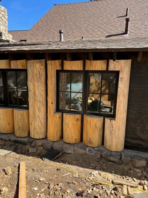 Exterior view of a building with windows framed by vertical wooden logs. Brown roof, blue sky.