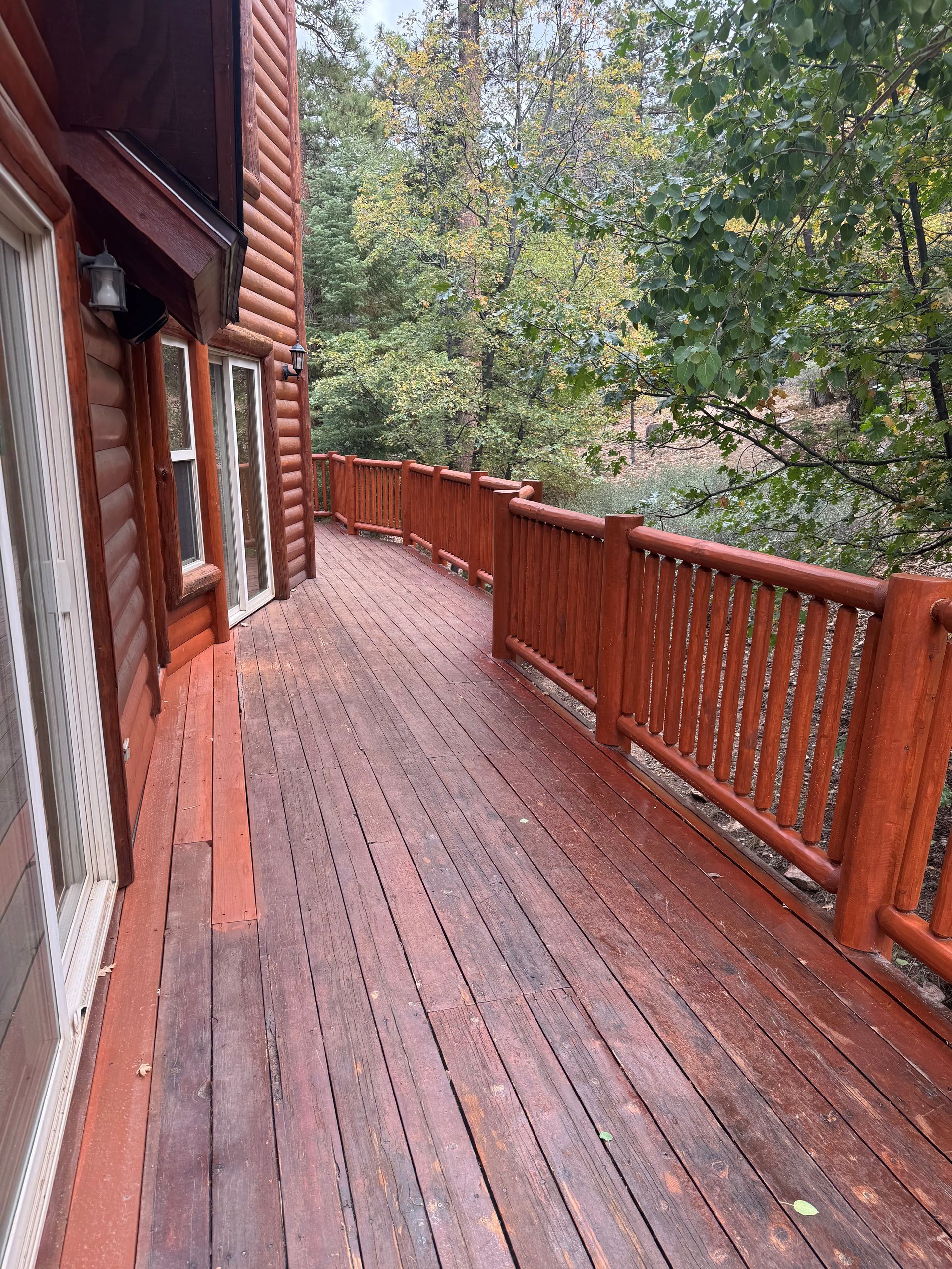 Wooden deck with reddish-brown stain on a log cabin-style house, surrounded by trees.
