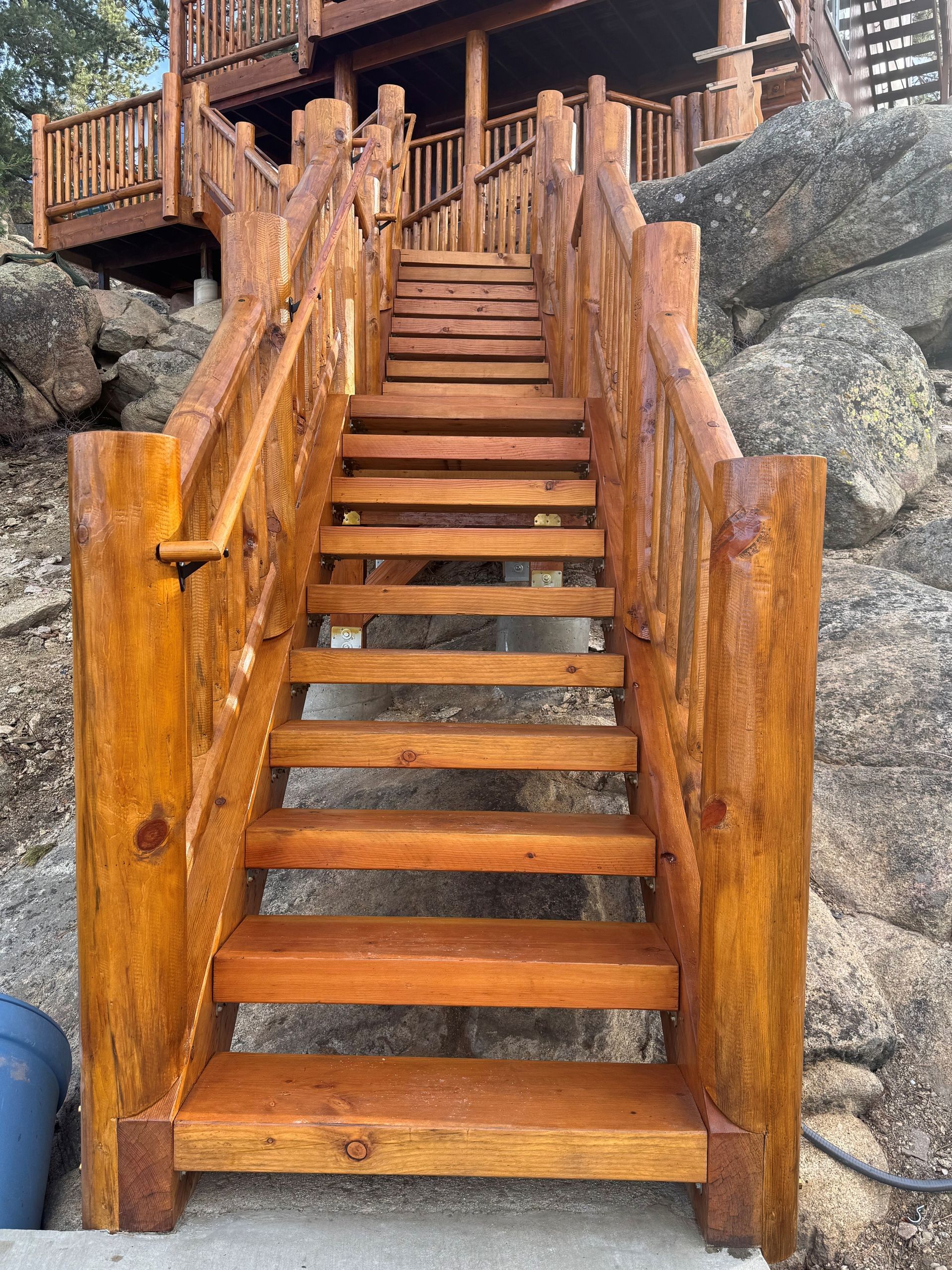 Wooden outdoor staircase leading up to a cabin, surrounded by rocks.