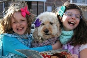 Two young girls are holding a dog and reading a magazine.