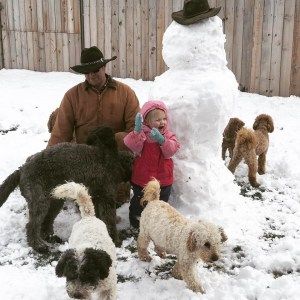 A man and a little girl are playing in the snow with their dogs.