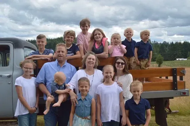 A large family is posing for a picture in the back of a truck.