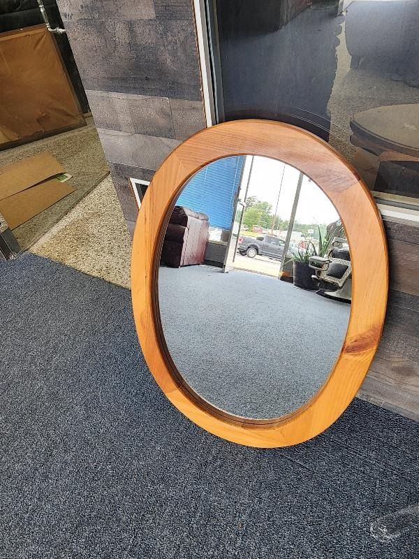 A round mirror with a wooden frame is sitting on a carpet.