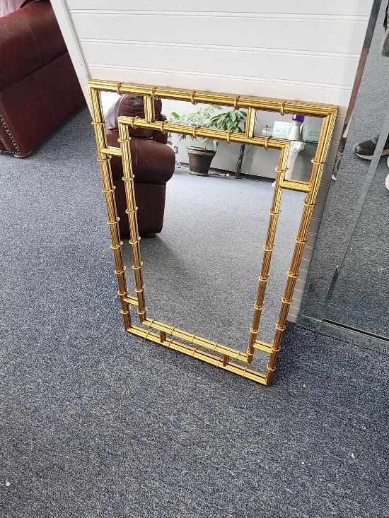 A gold framed mirror is sitting on a carpeted floor in a living room.