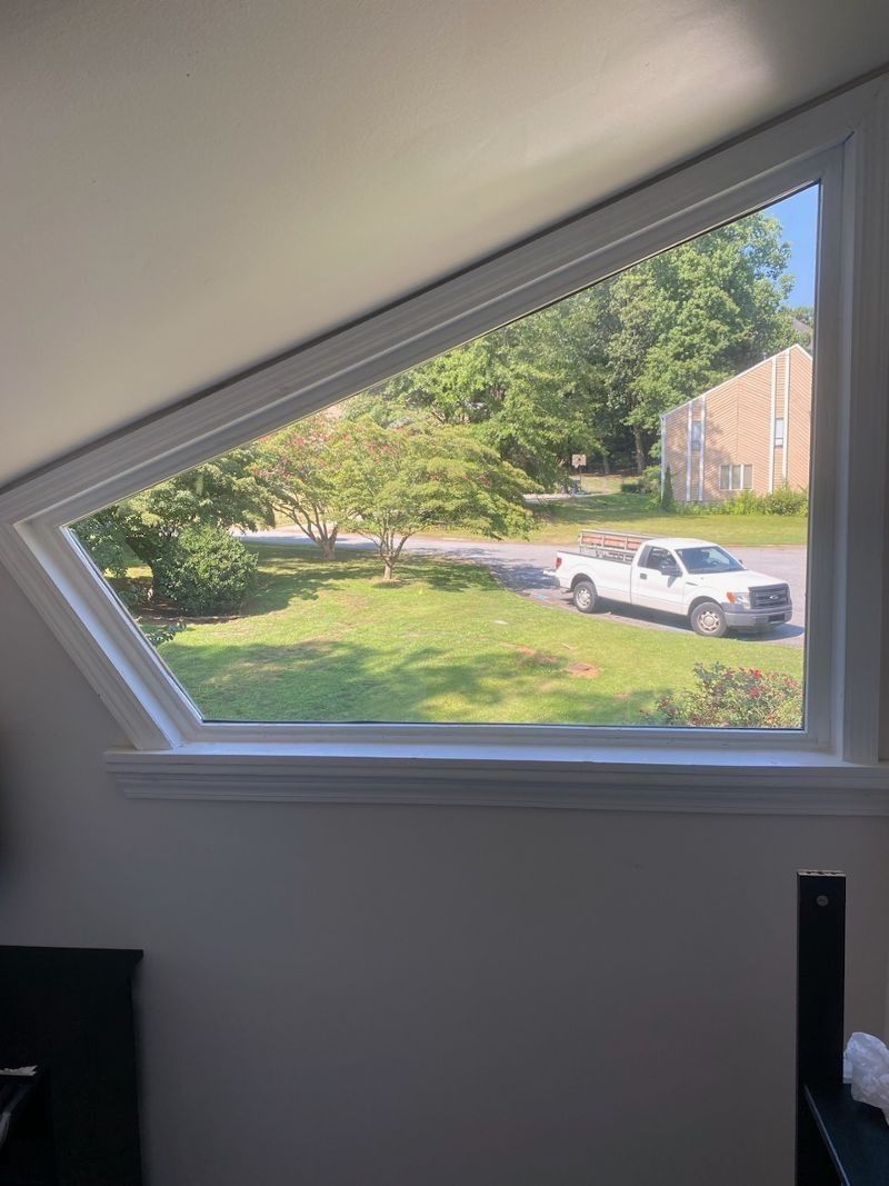 A white truck is parked in the grass in front of a window.