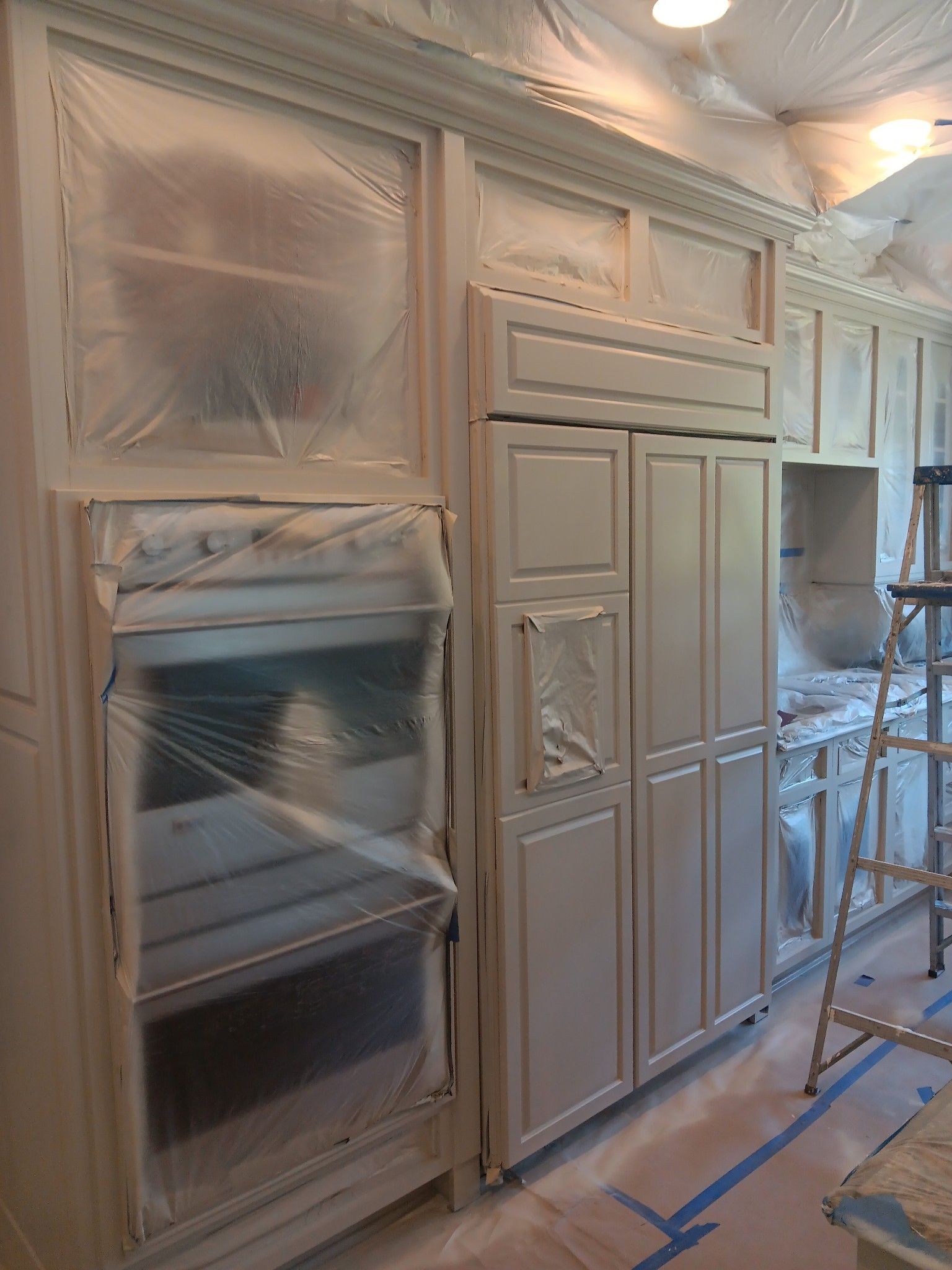 A kitchen with white cabinets and a refrigerator is being painted.